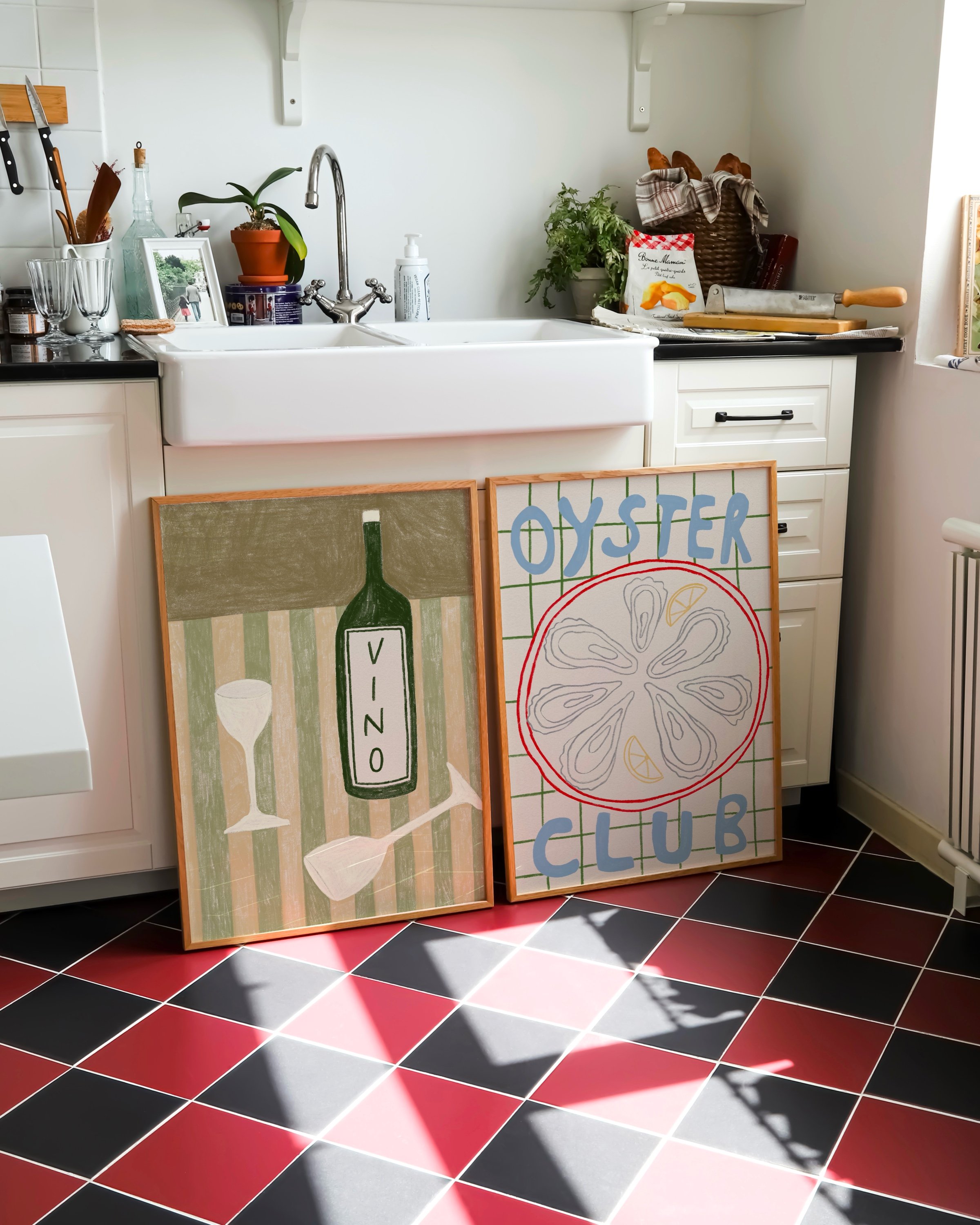 Two framed art prints: one featuring a colorful oyster illustration with the text ‘Oyster Club’ and another showcasing a green wine bottle labeled ‘Vino’ with glasses on a striped background.