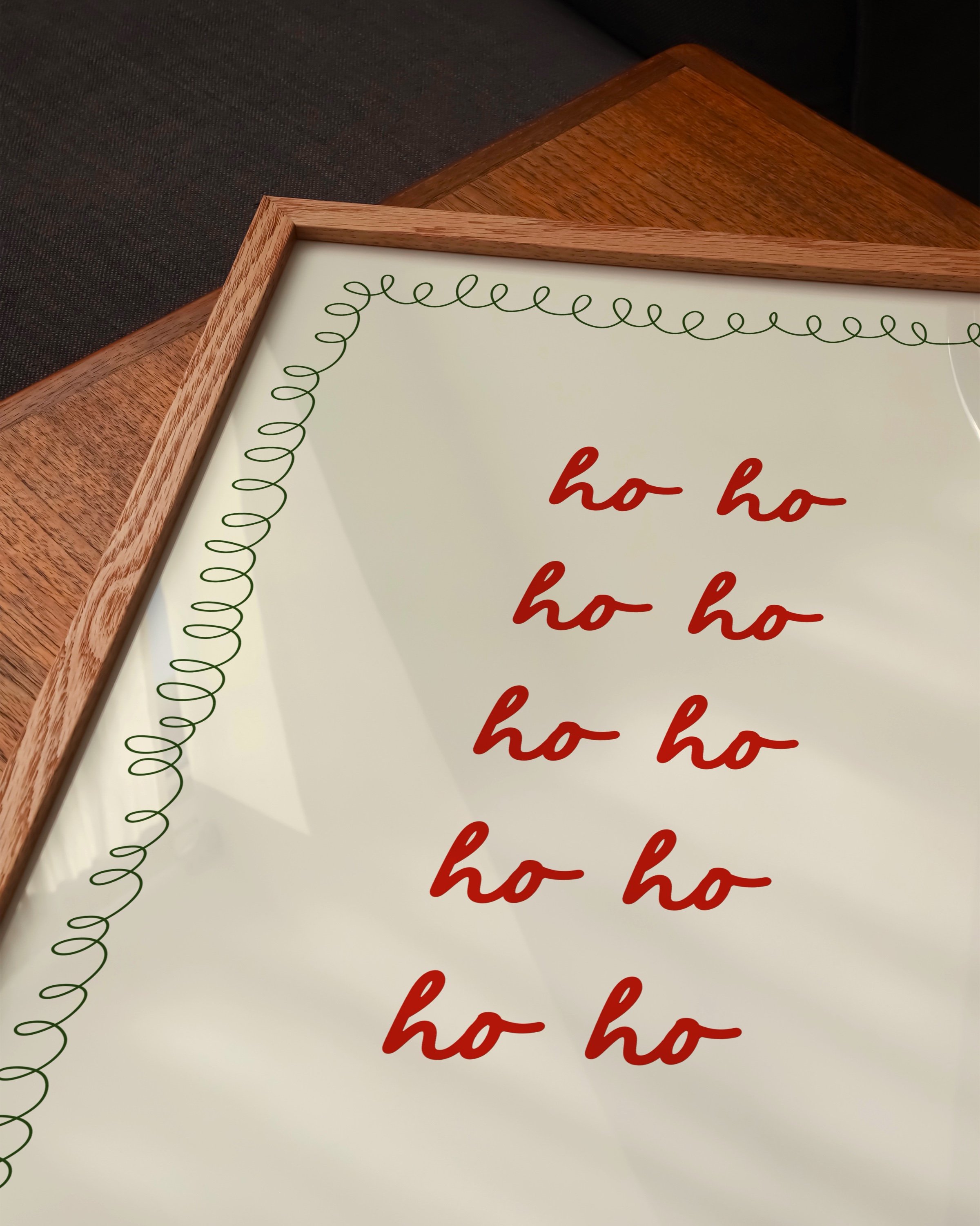 Christmas printable art with repeated red ‘Ho Ho Ho’ text in a handwritten style, framed by a green squiggle border on a beige background.