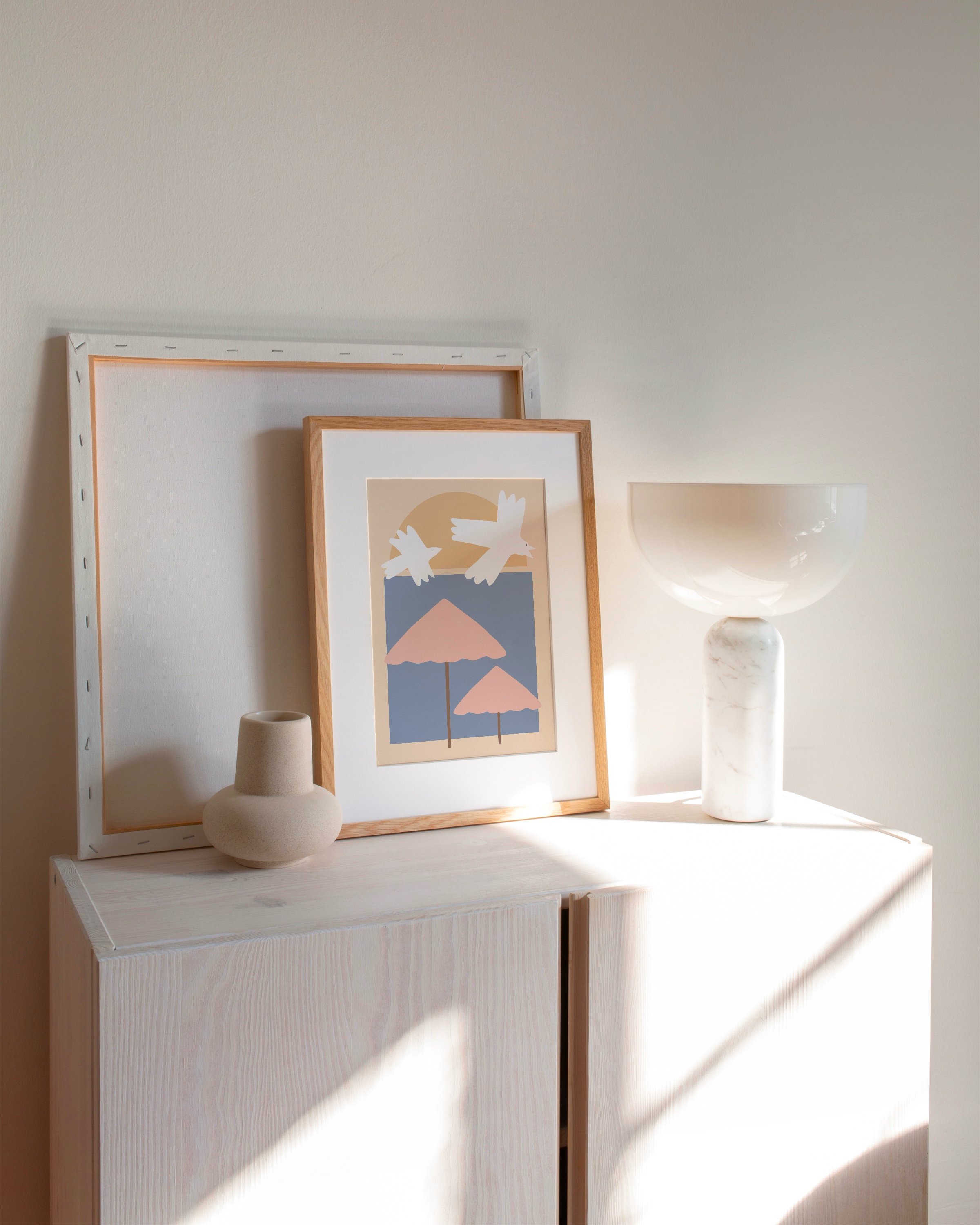 Printable wall art featuring a minimalist illustration of pink beach umbrellas and white seagulls against a soft blue and peach background.
