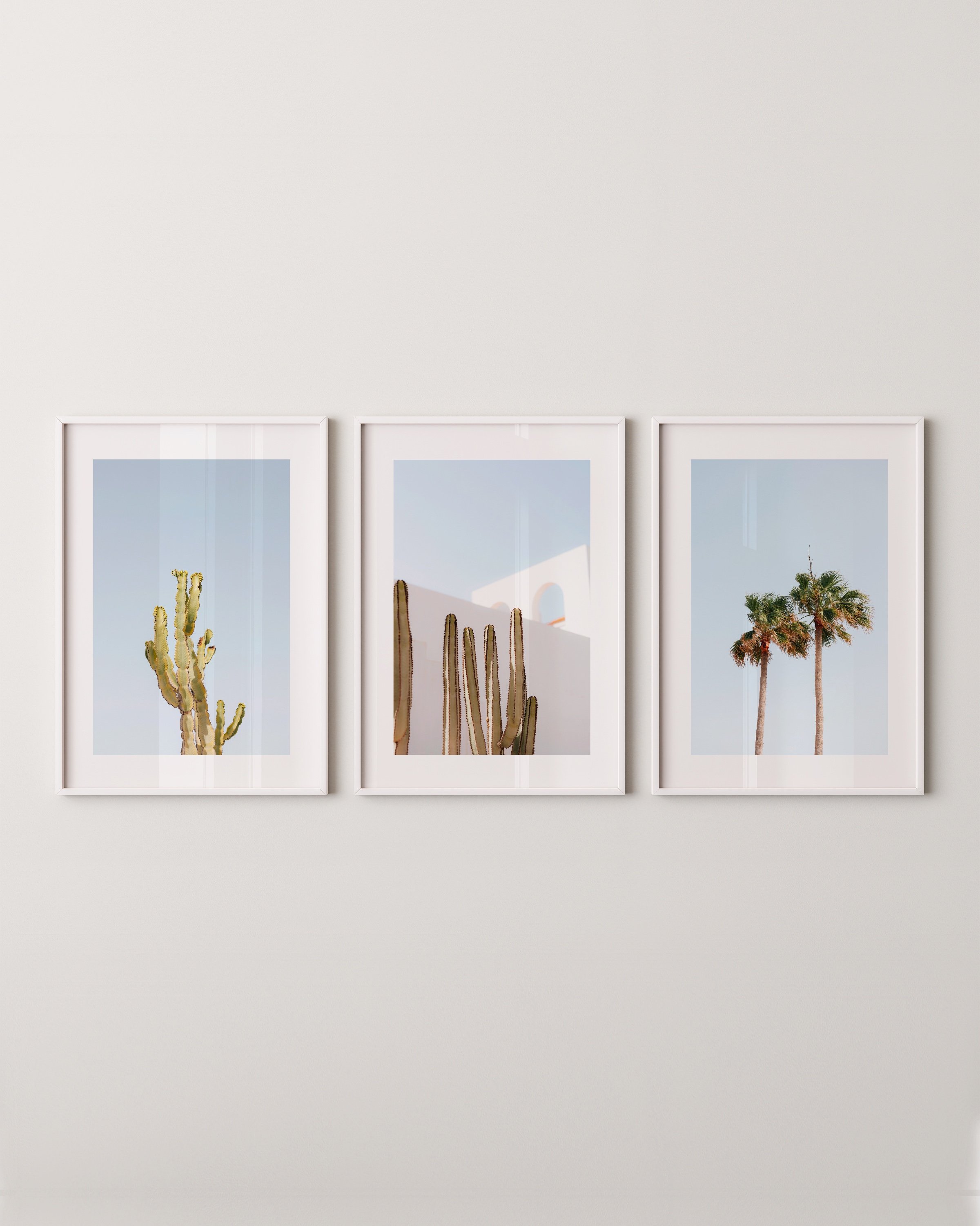 Set of three desert-themed wall art prints featuring cacti, palm trees, and minimalist architecture under a bright blue sky.