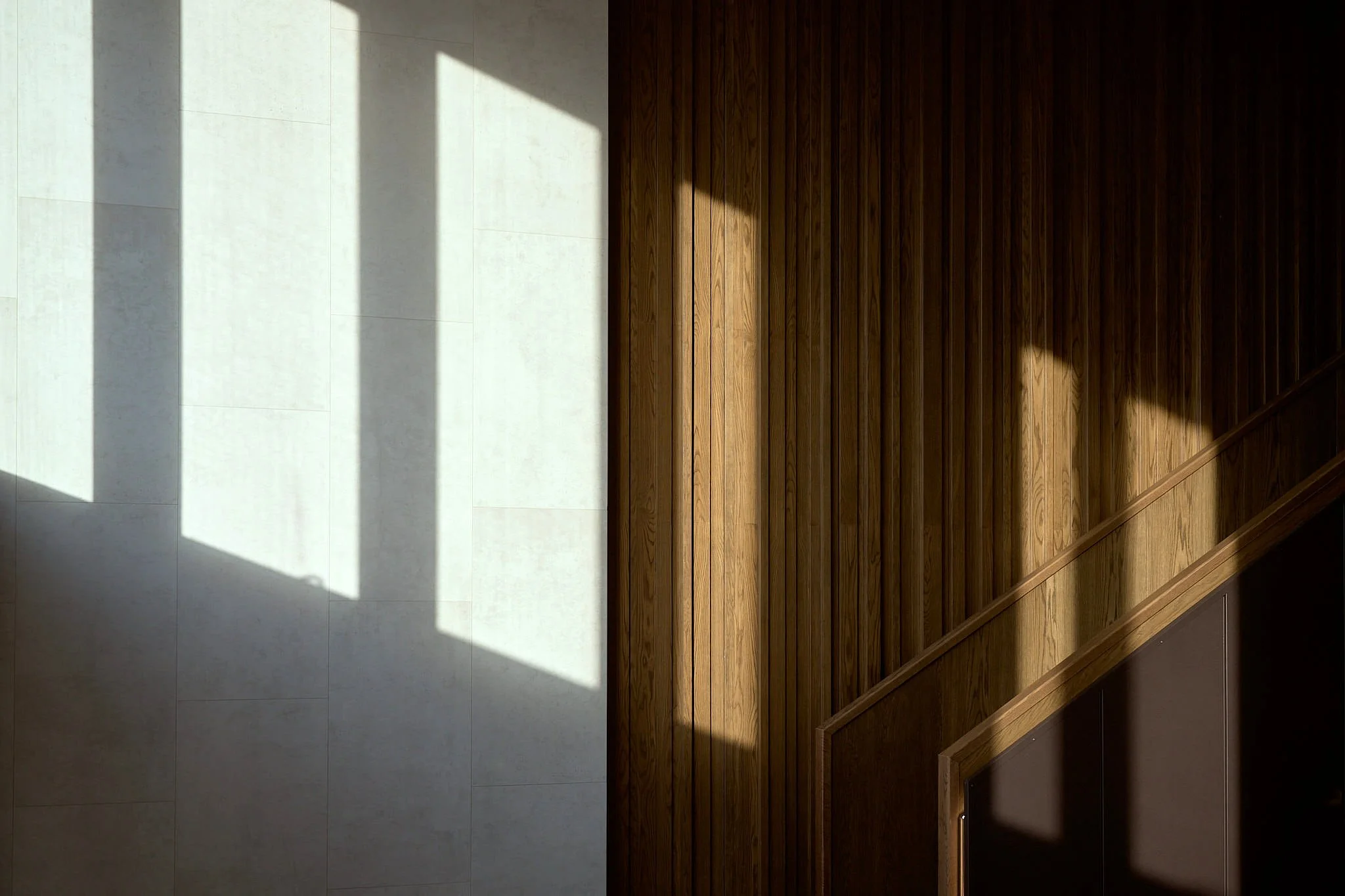 Sunlight casting shadows on a tiled wall and wooden staircase wall.