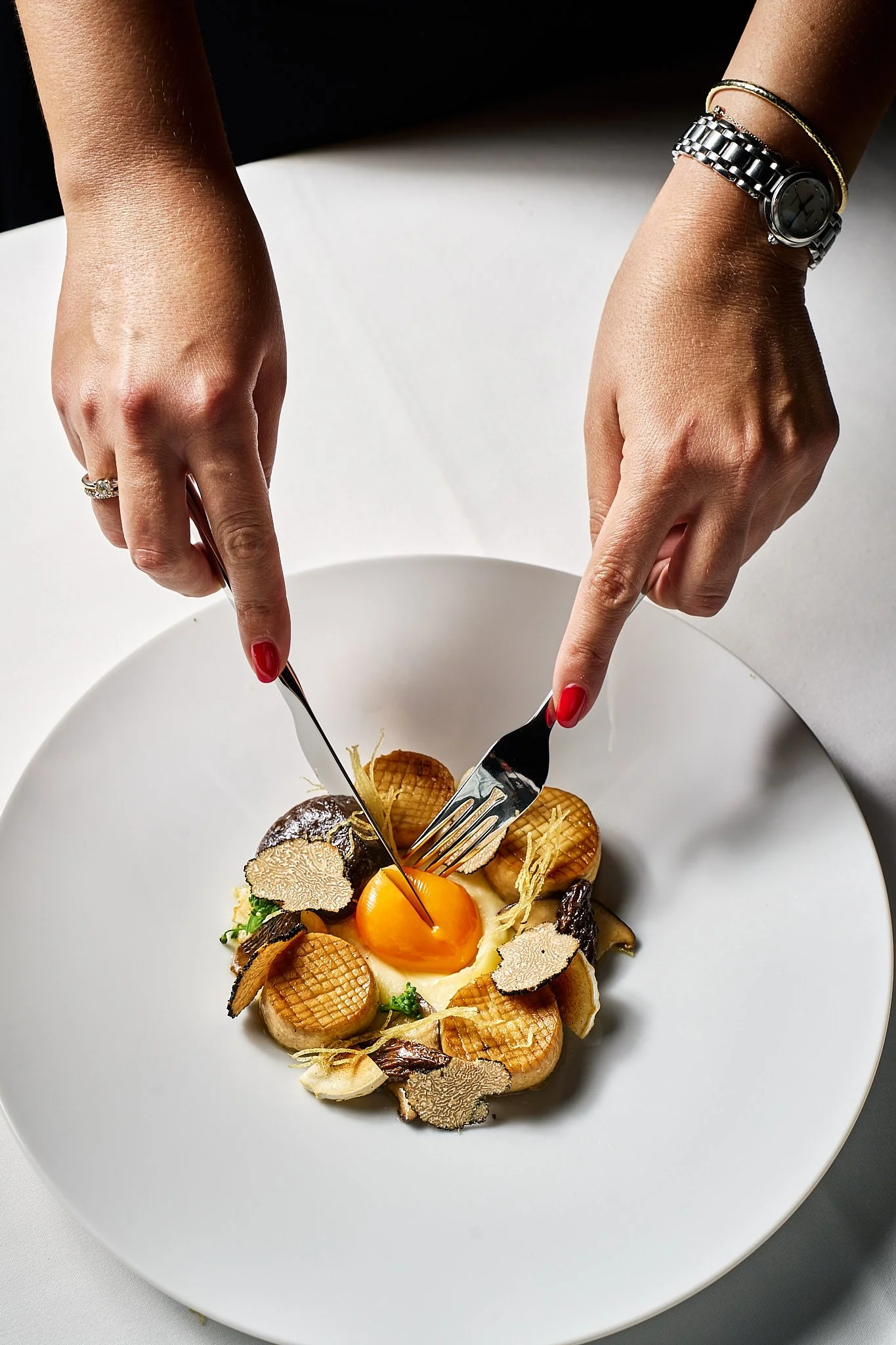 Person preparing a gourmet dish with a yolk, truffles, and other ingredients on a white plate.