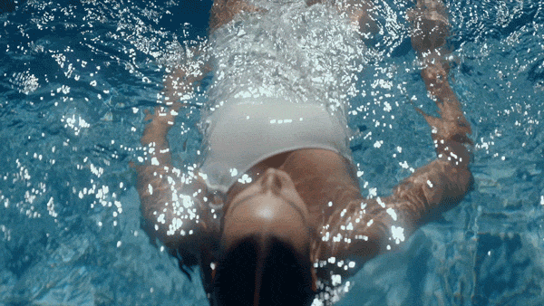 Person floating on their back in a swimming pool with arms outstretched.
