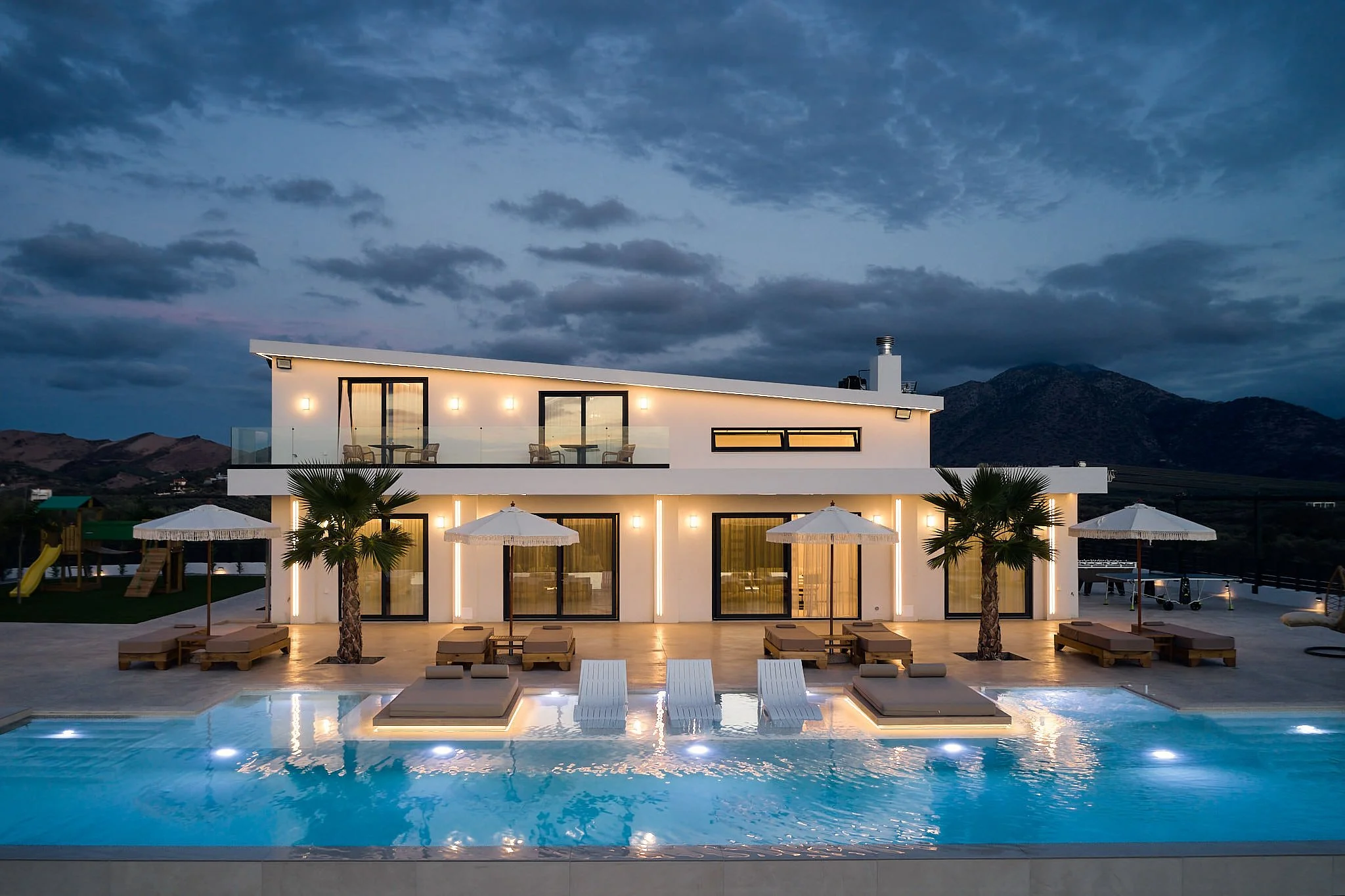 Modern two-story house with outdoor pool and lounge chairs at twilight.