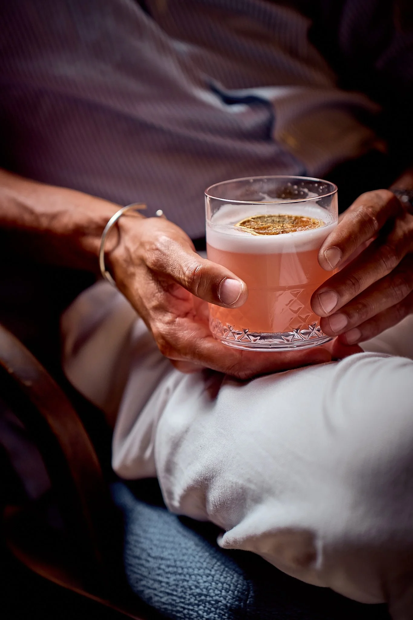 Person holding a glass of pink cocktail garnished with a slice of lime.