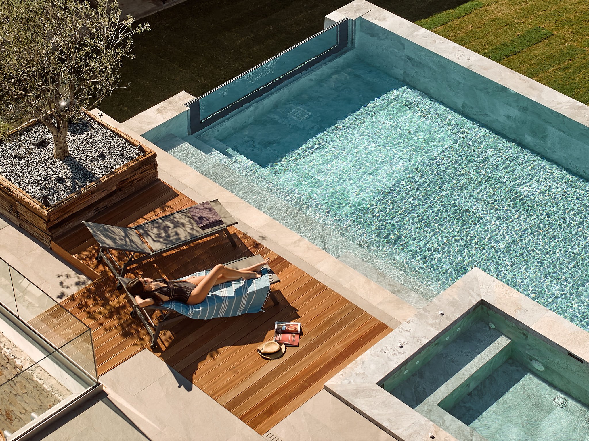 A woman lounging on a chair next to a swimming pool with a small hot tub in a backyard