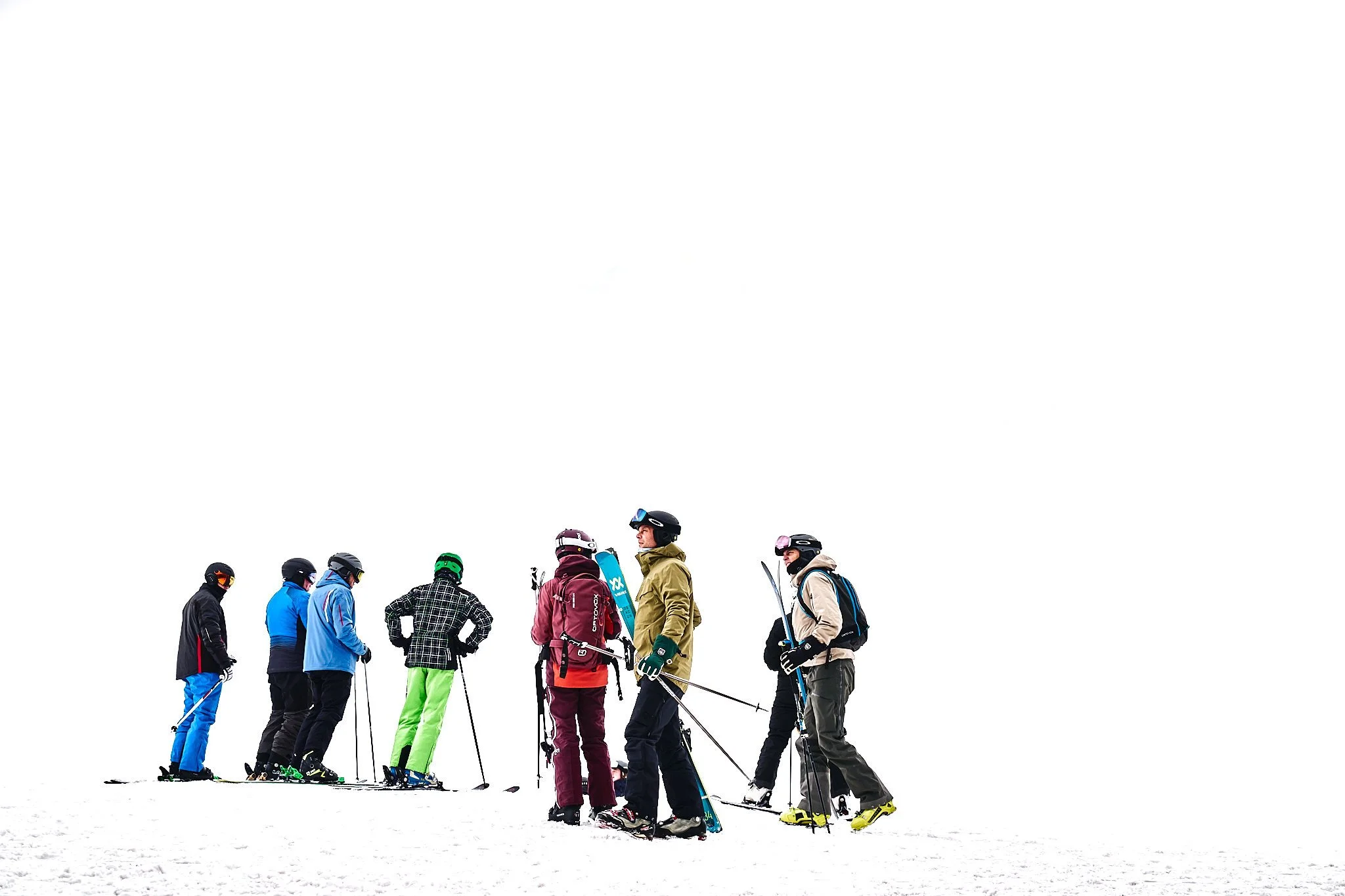 Group of skiers standing on snow, dressed in colorful winter gear, preparing to ski in a snowy landscape.