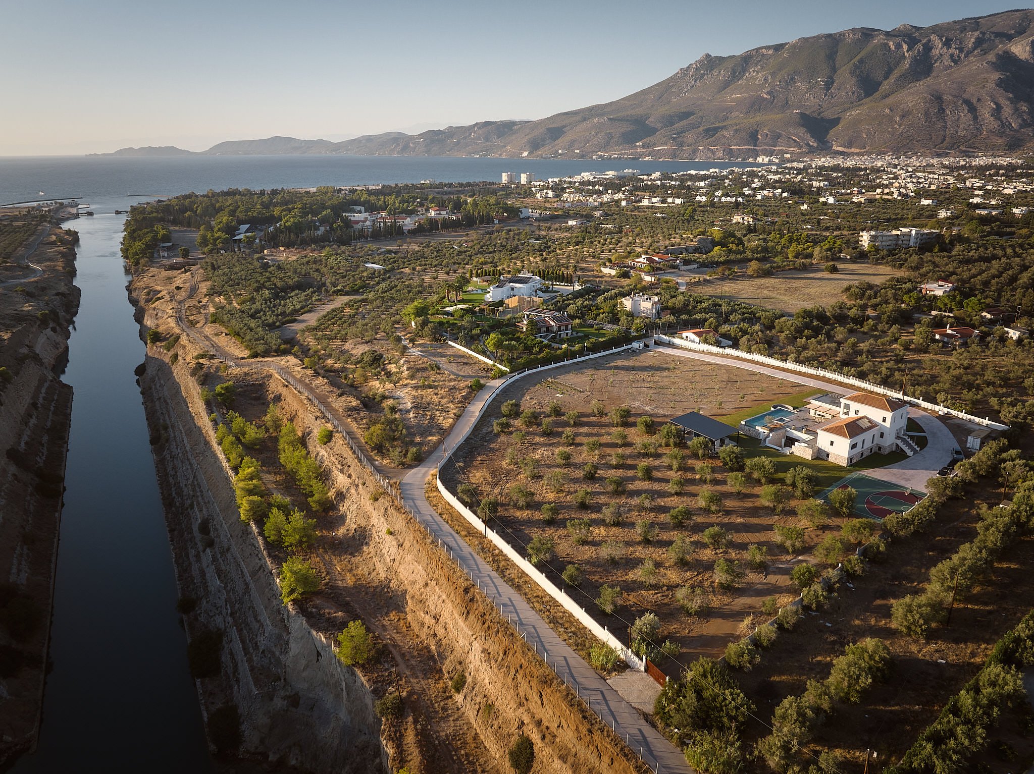 Aerial view of a coastline with cliffs and waterway, residential houses, and green farmland near mountains in the background.