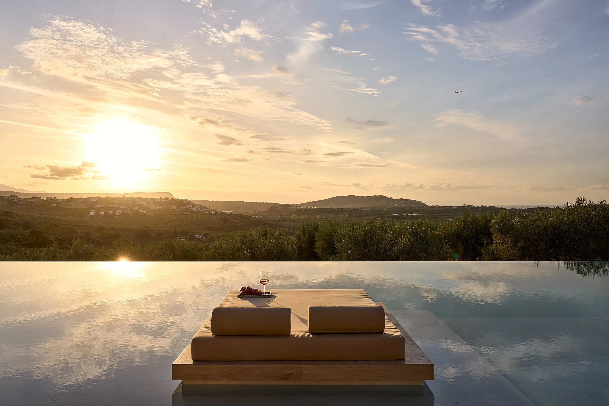 Infinity pool overlooking a sunset with a glass of wine and grapes on a tray.