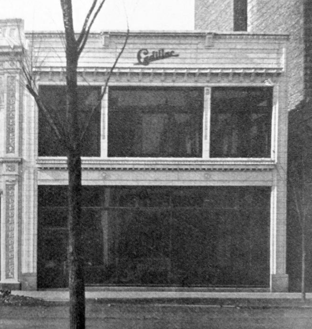 A vintage black and white photograph of a two-story building with wide windows, a canopy, and a sign that reads 'Gallace' on the top. A tree is in front of the building.
