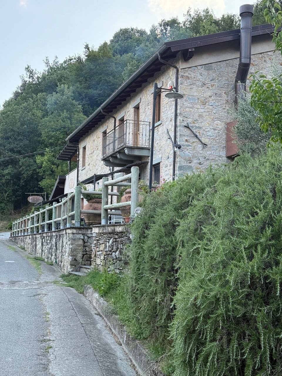 stone farmhouse with wooden balcony surrounded by hillside greenery in tuscany