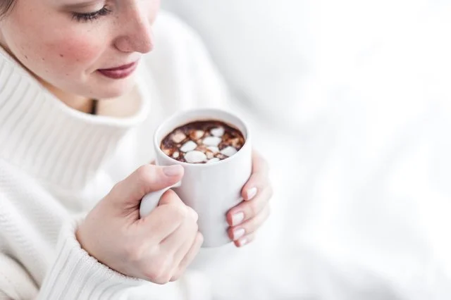 A soft winter scene of a woman in a cream sweater holding a warm mug of hot chocolate, captured in bright, gentle natural light.