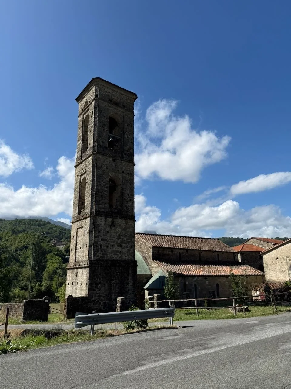 stone bell tower standing beside rustic buildings in the tuscan countryside