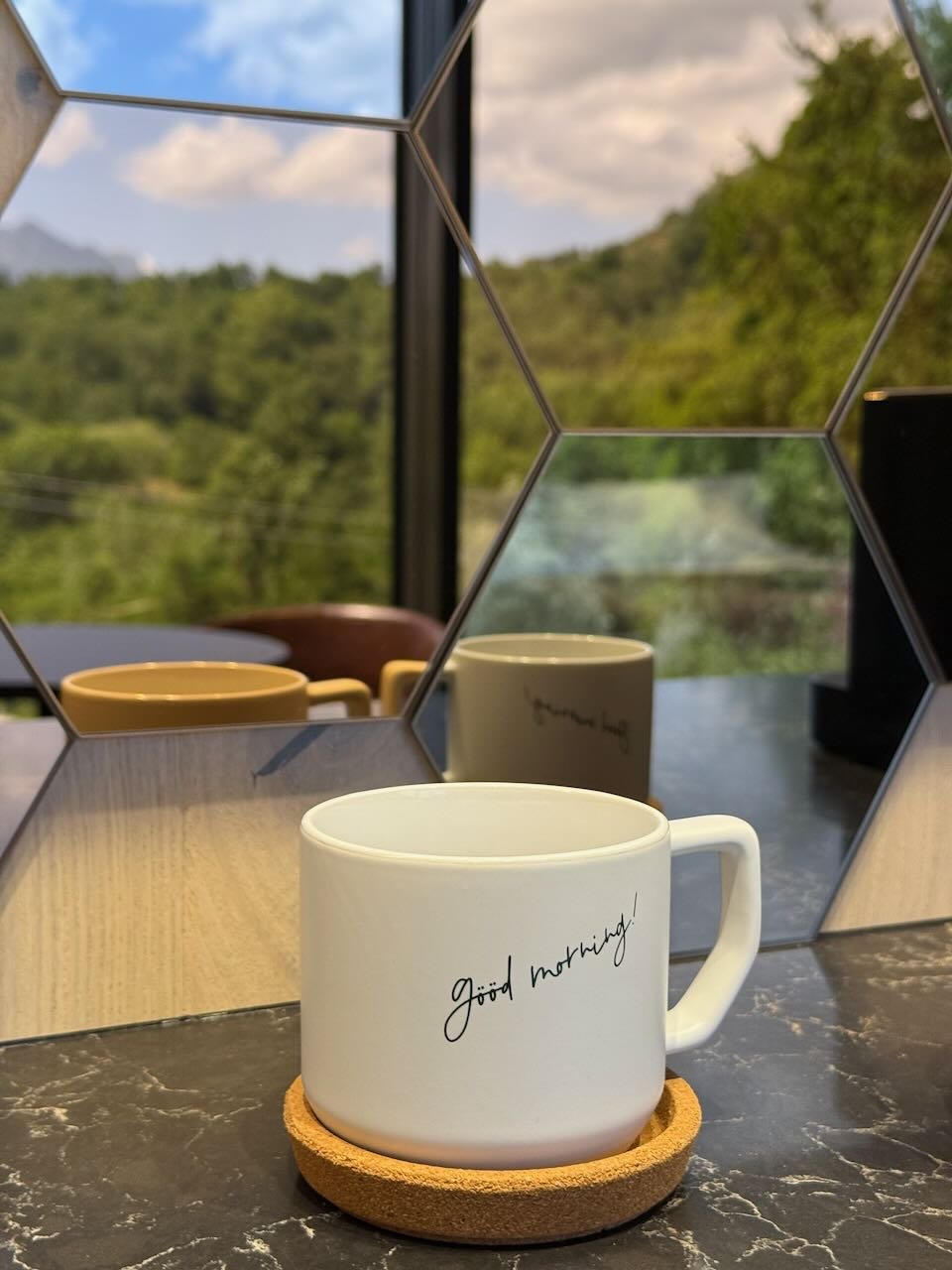 white mug on a table beside mirrored window reflecting trees and sky in tuscany