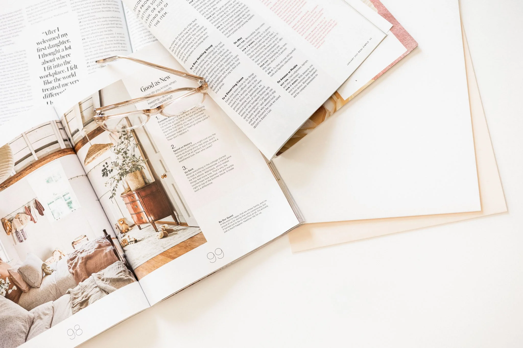 Open magazine pages with neutral tones and reading glasses resting across the layout, styled on a bright workspace — soft, quiet editorial imagery for a creative lifestyle article.