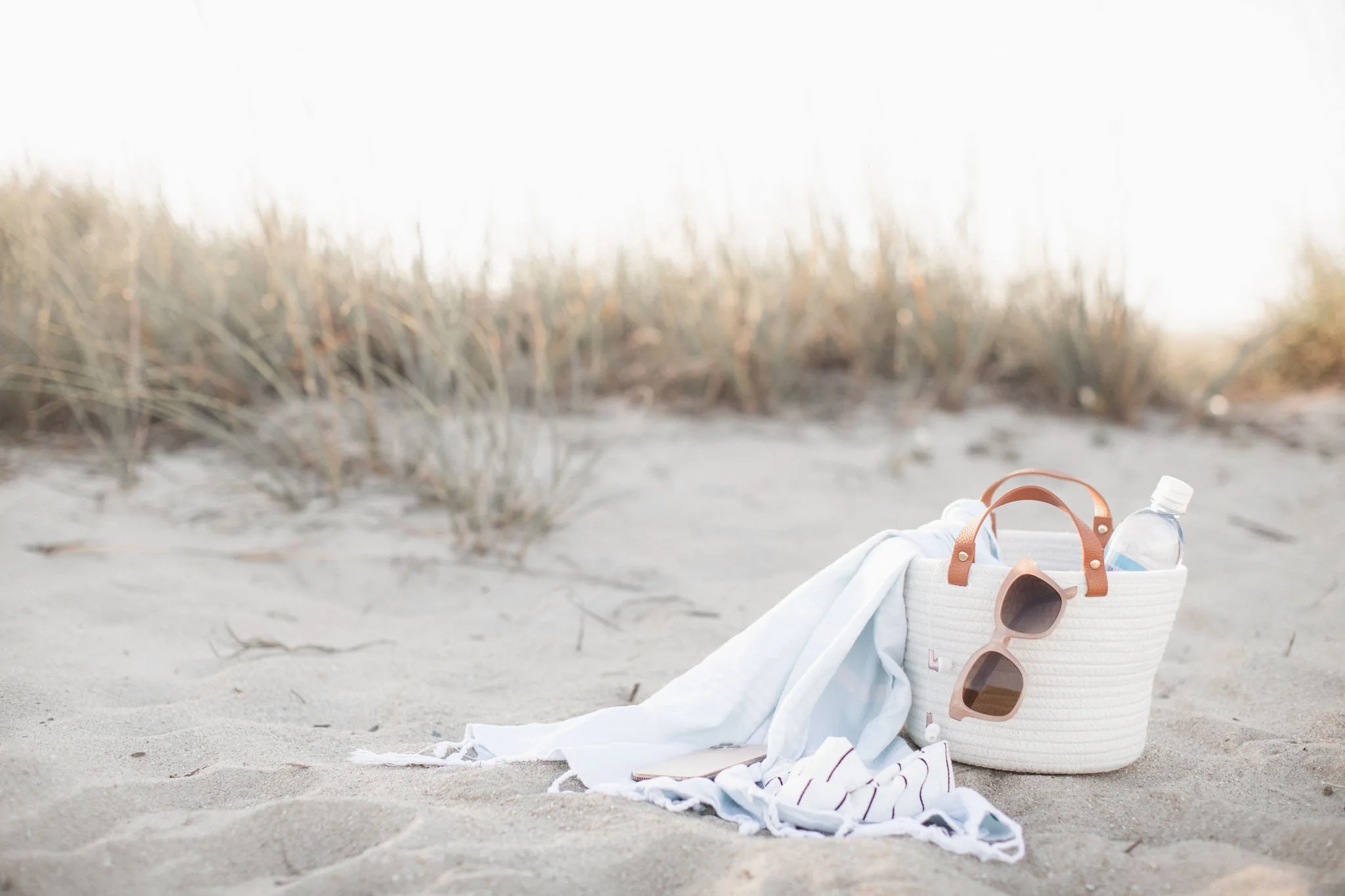 A minimalist white travel bag resting on soft sand, sunglasses and light textiles draped beside it — a calm symbol of creative work done from anywhere.