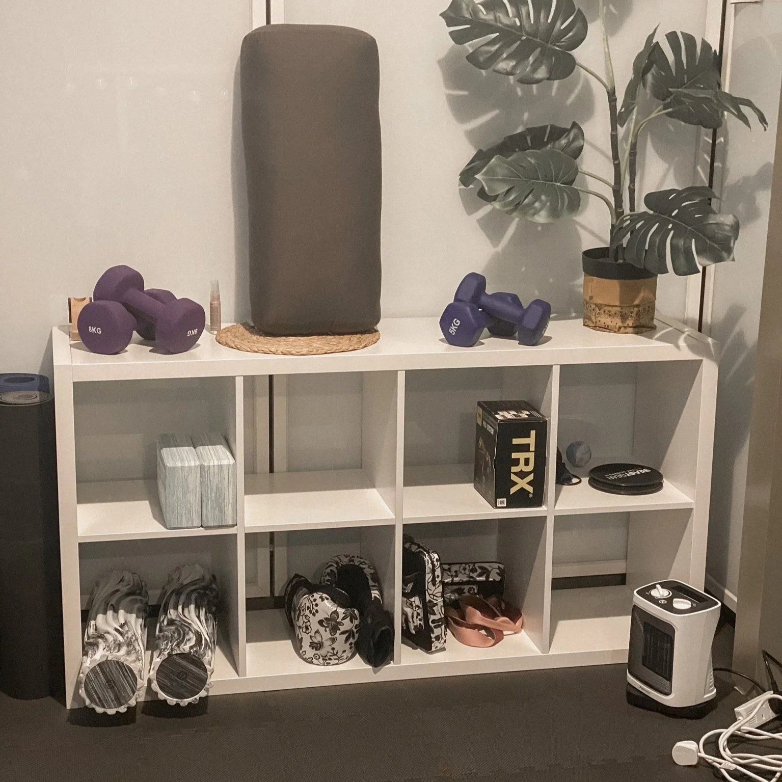 Organised small-home gym storage with white shelving, neutral equipment, and soft warm lighting