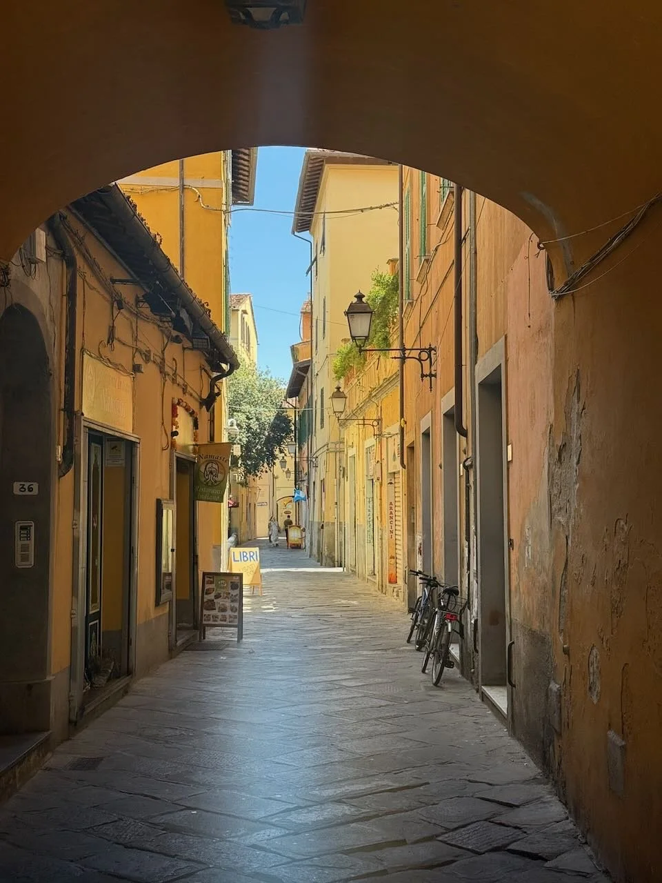narrow cobblestone street with yellow buildings and bicycles under an archway in italy