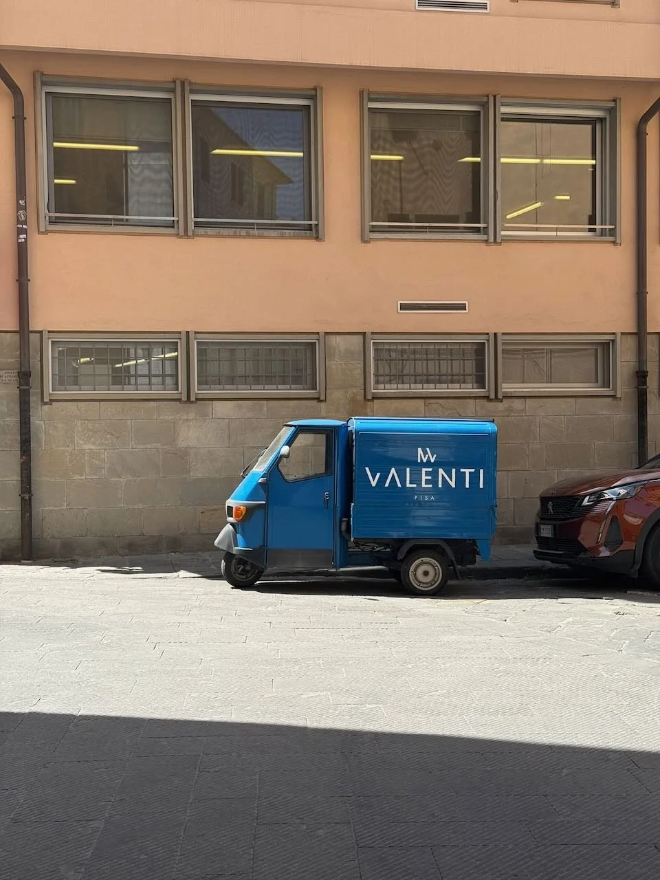 blue three wheeled delivery truck parked beside a stone building in italy