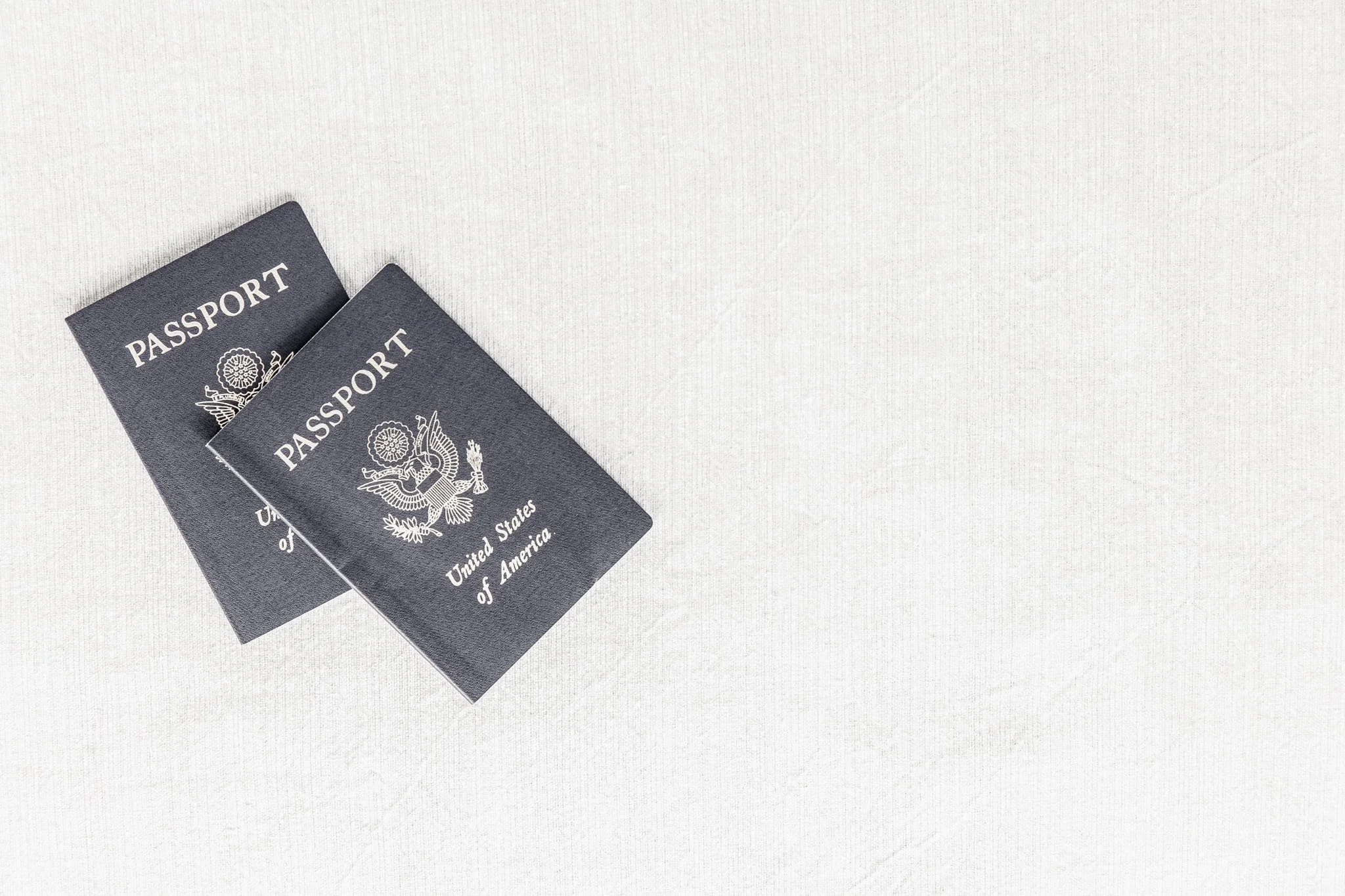 Two navy United States passports placed on a soft light-grey fabric background — minimal, calm and visually spacious, representing global mobility and cross-border work for creatives.
