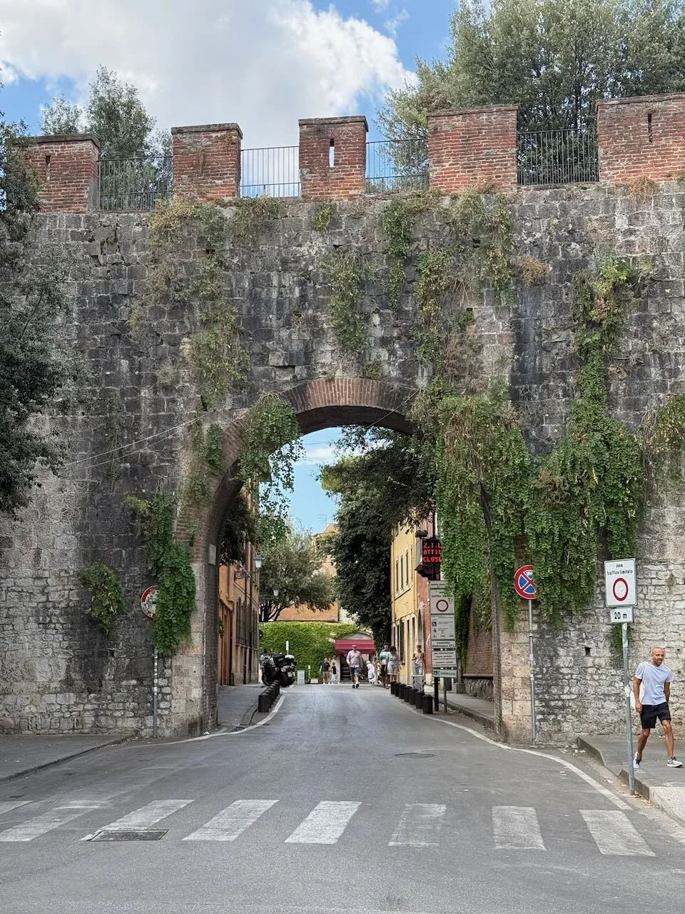 historic stone gate covered in greenery leading into a street in italy