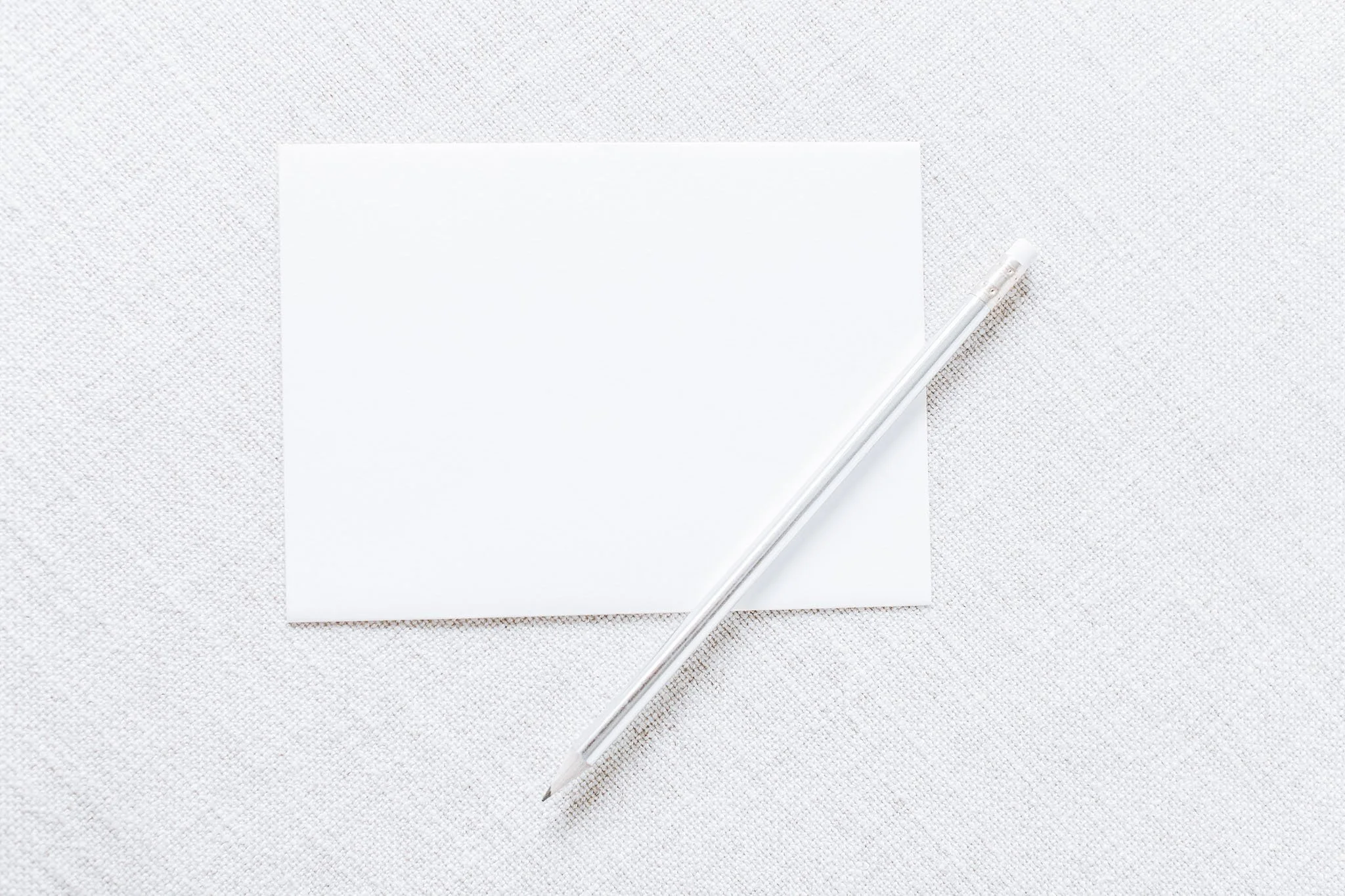 A minimal flat-lay of a blank white note card and a gold pencil on a soft, textured surface — symbolising clarity, intention and the beginning of a brand.