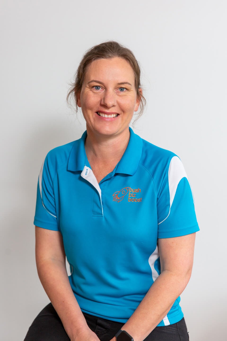 Founder of Bush Biz Boost, Amy Treacy, is pictured in her blue uniform sitting on a stool and smiling warmly.