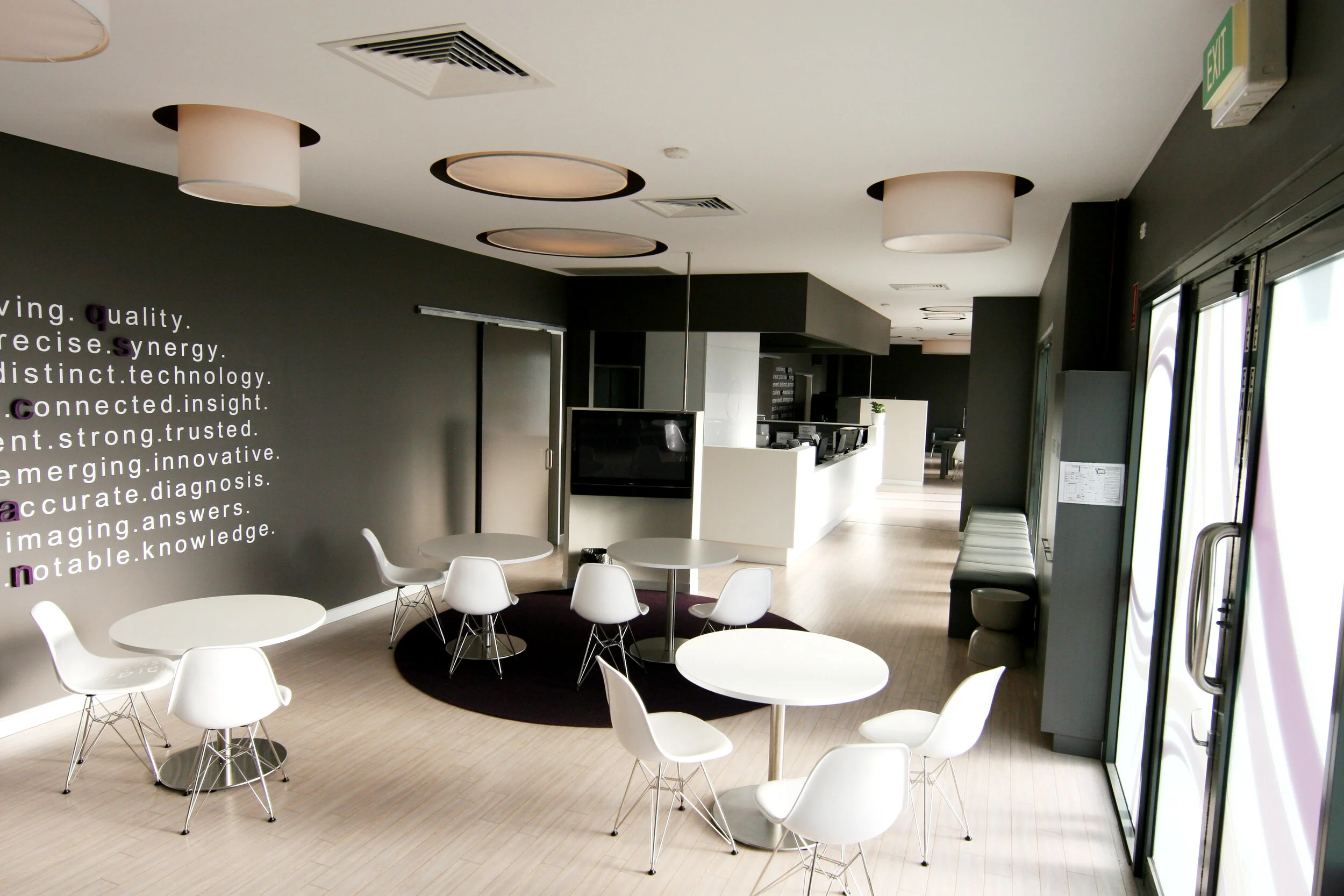Modern cafe or lounge with white chairs and tables, black accent wall with words, and a front door with a glass window.