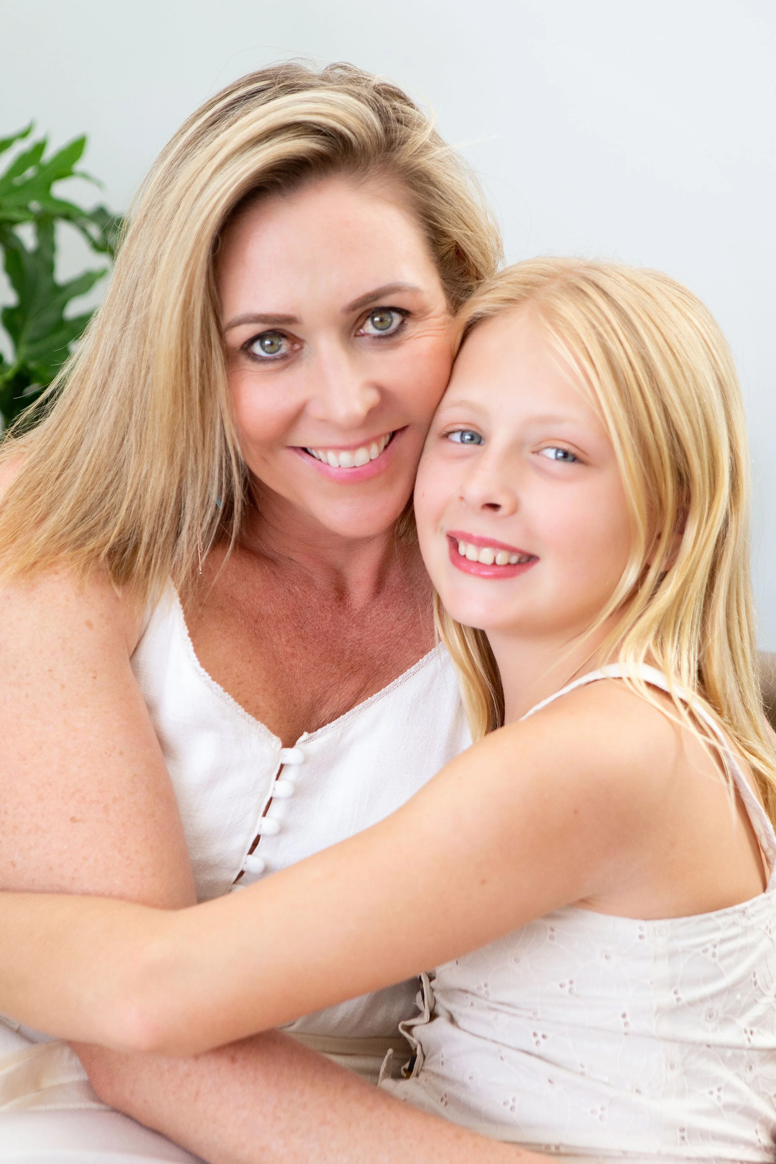 A woman and a young girl smiling and hugging each other indoors.