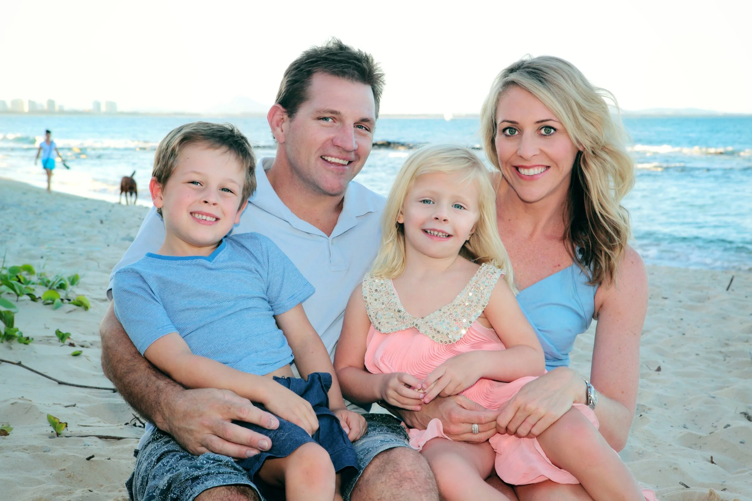 A smiling family of four sitting on a beach with the ocean in the background.