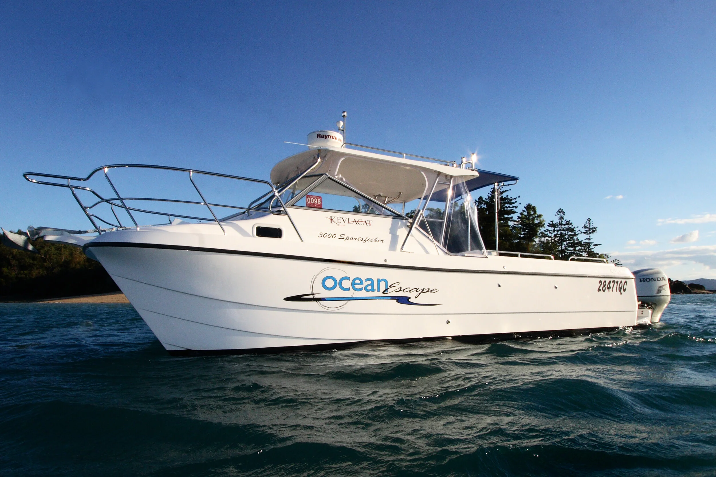 A white motorboat named Ocean Escape on the water with a land and trees background under a clear blue sky.