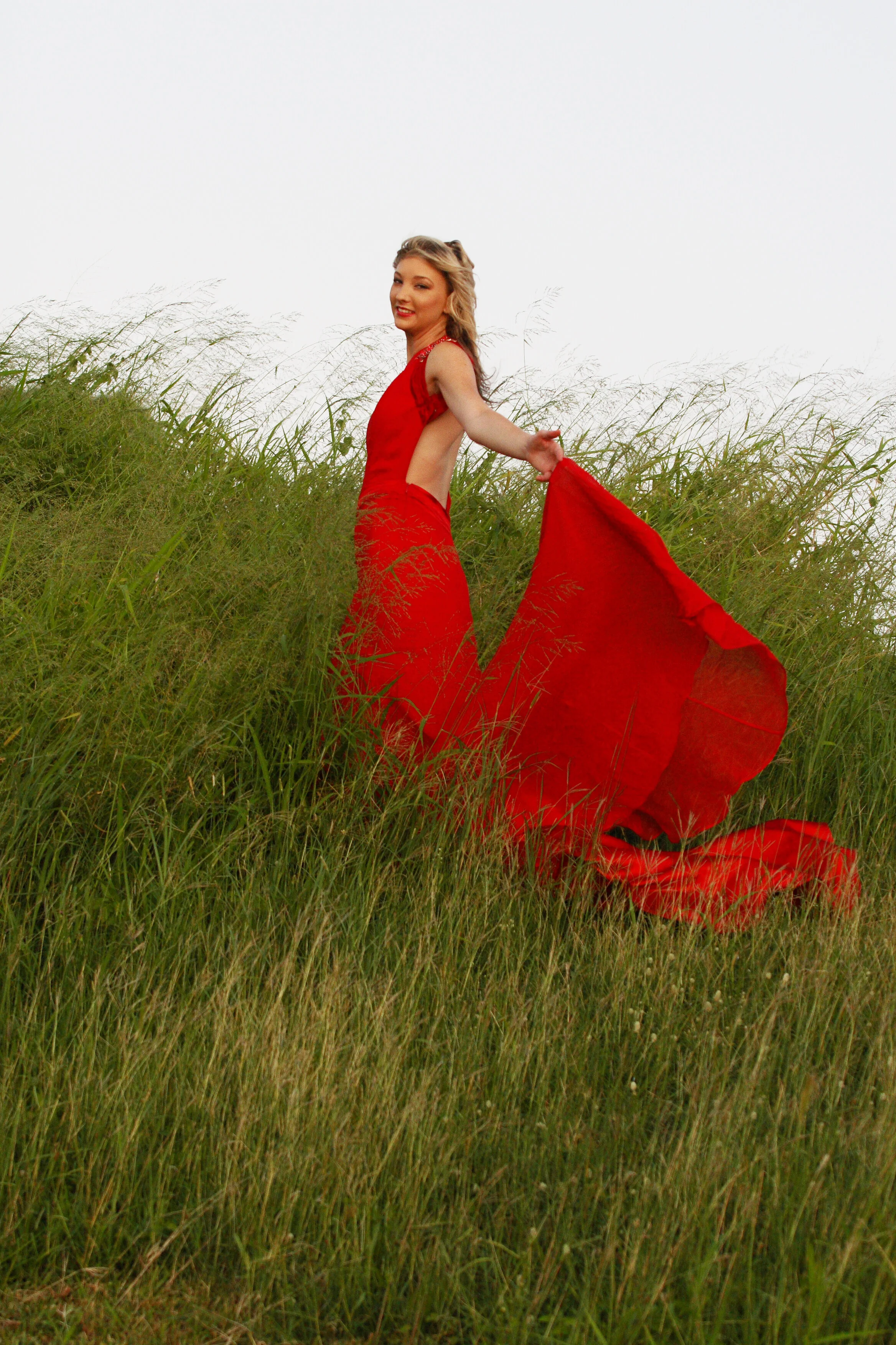 Woman in a flowing red dress standing in a grassy field, holding out the dress behind her, smiling.