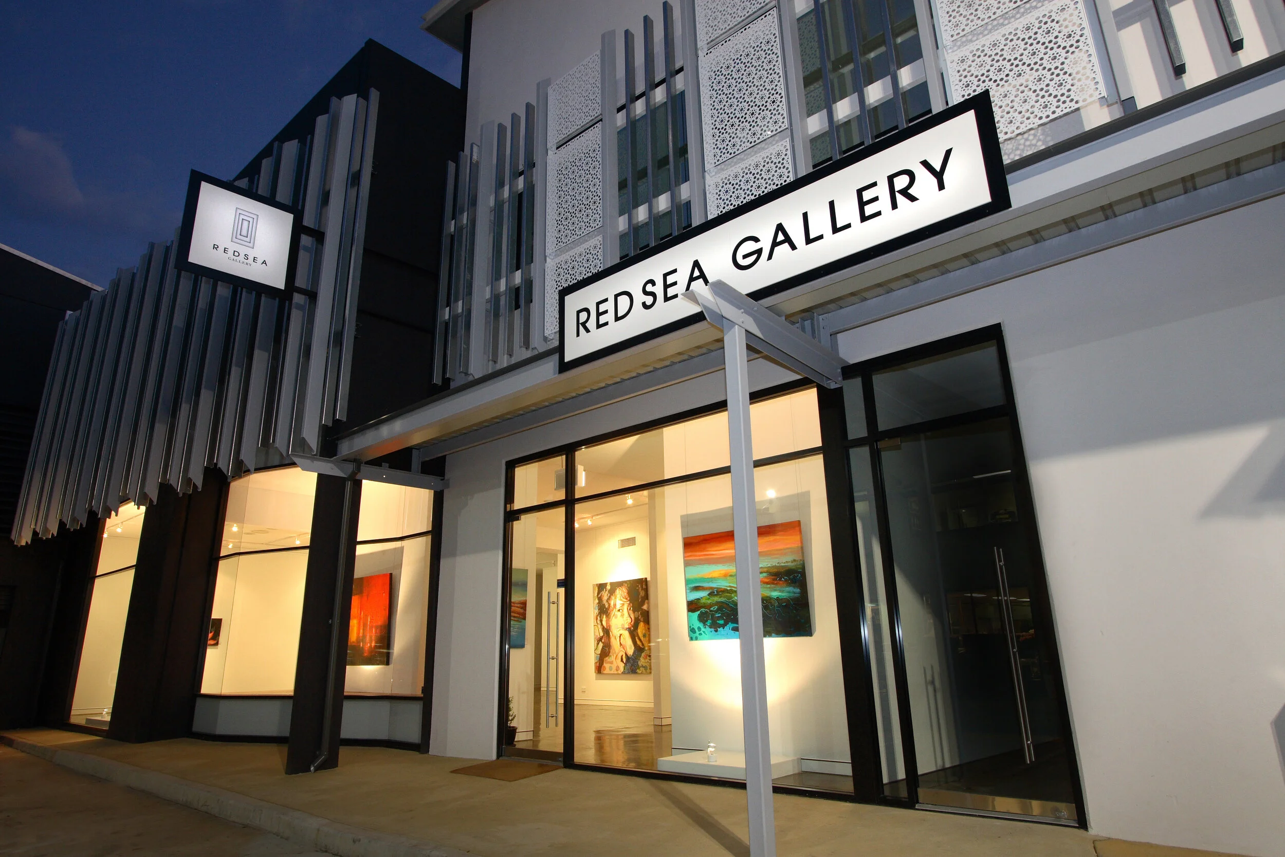 Exterior of the Red Sea Gallery, a modern art gallery with large glass windows displaying colorful paintings inside, and a sign that reads 'Red Sea Gallery' above the entrance.