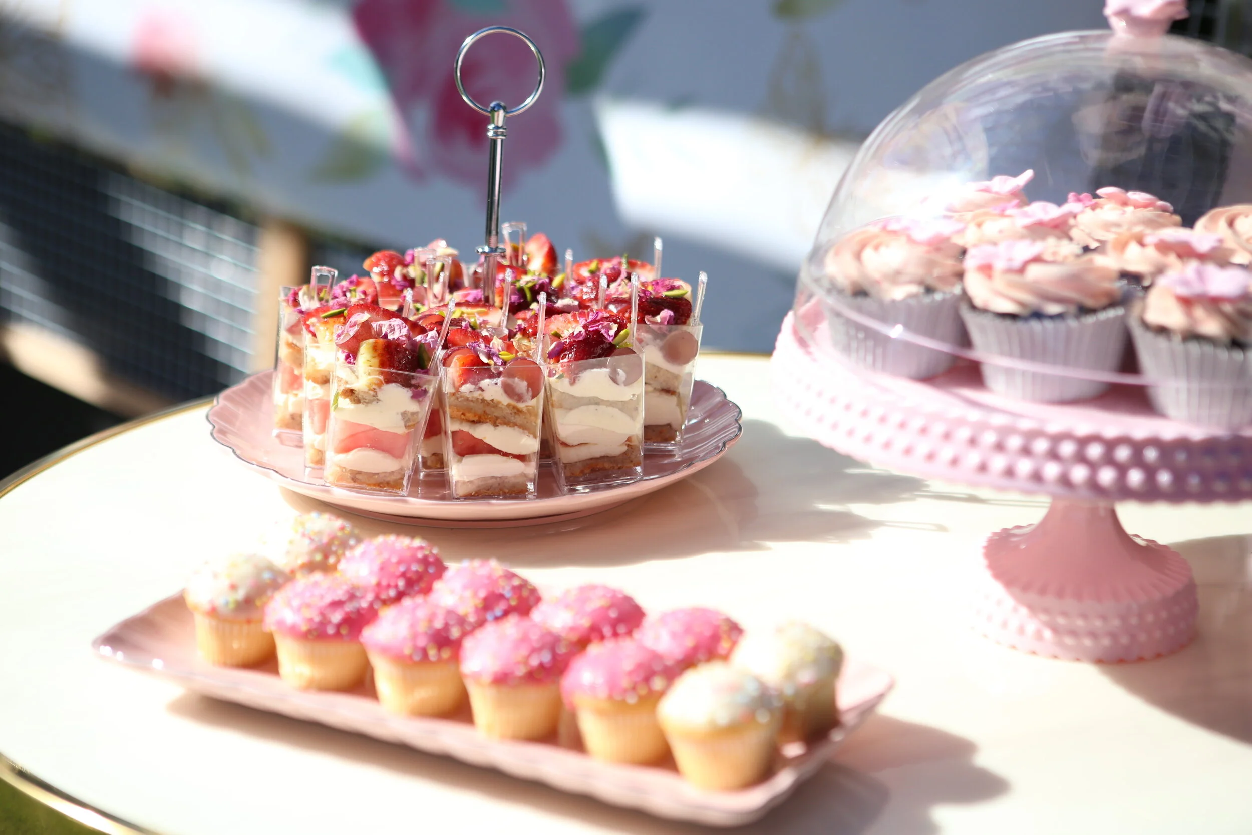 Assorted cupcakes and dessert slices on pink trays at a party