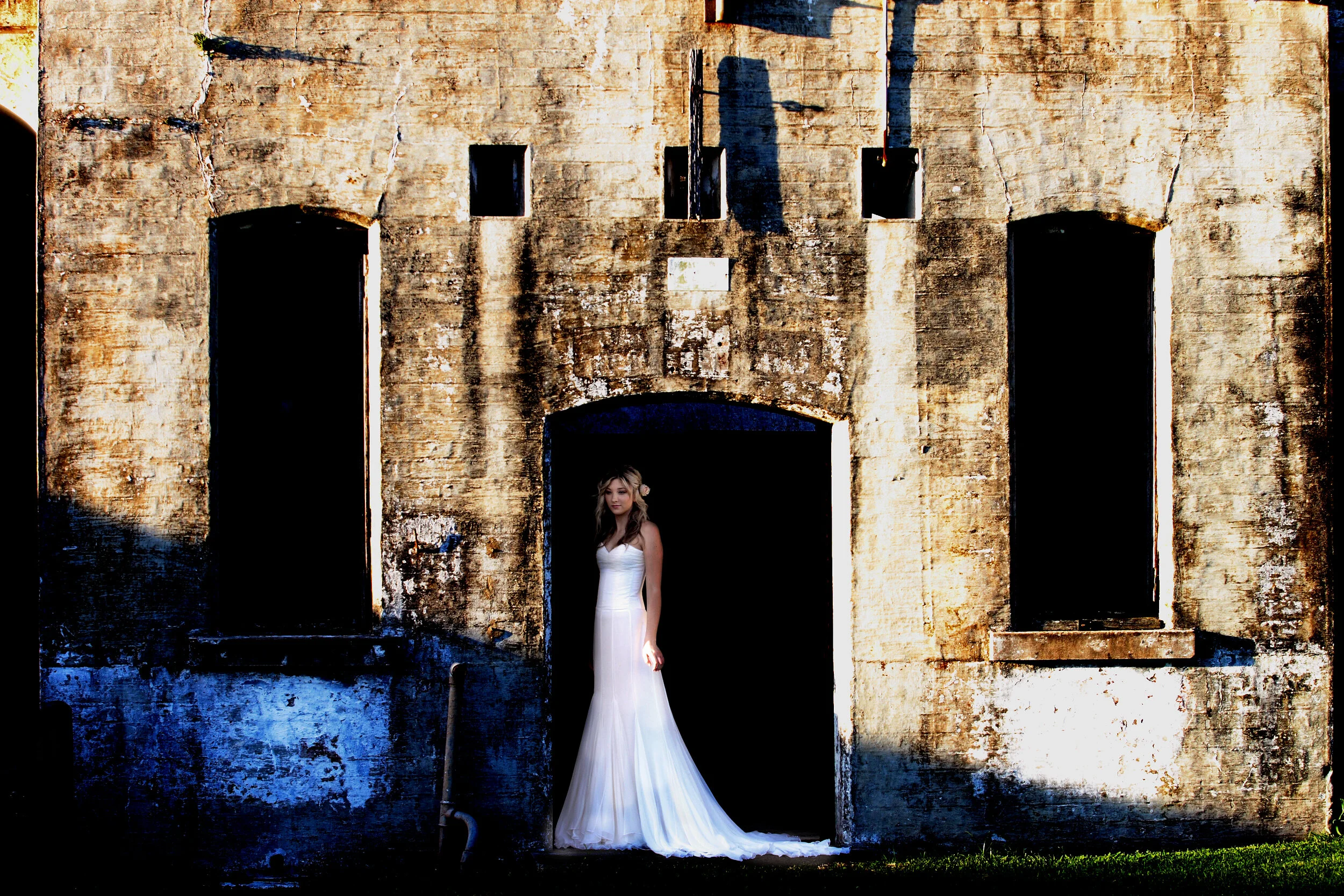 A woman in a white dress standing in the doorway of an old, weathered brick building.