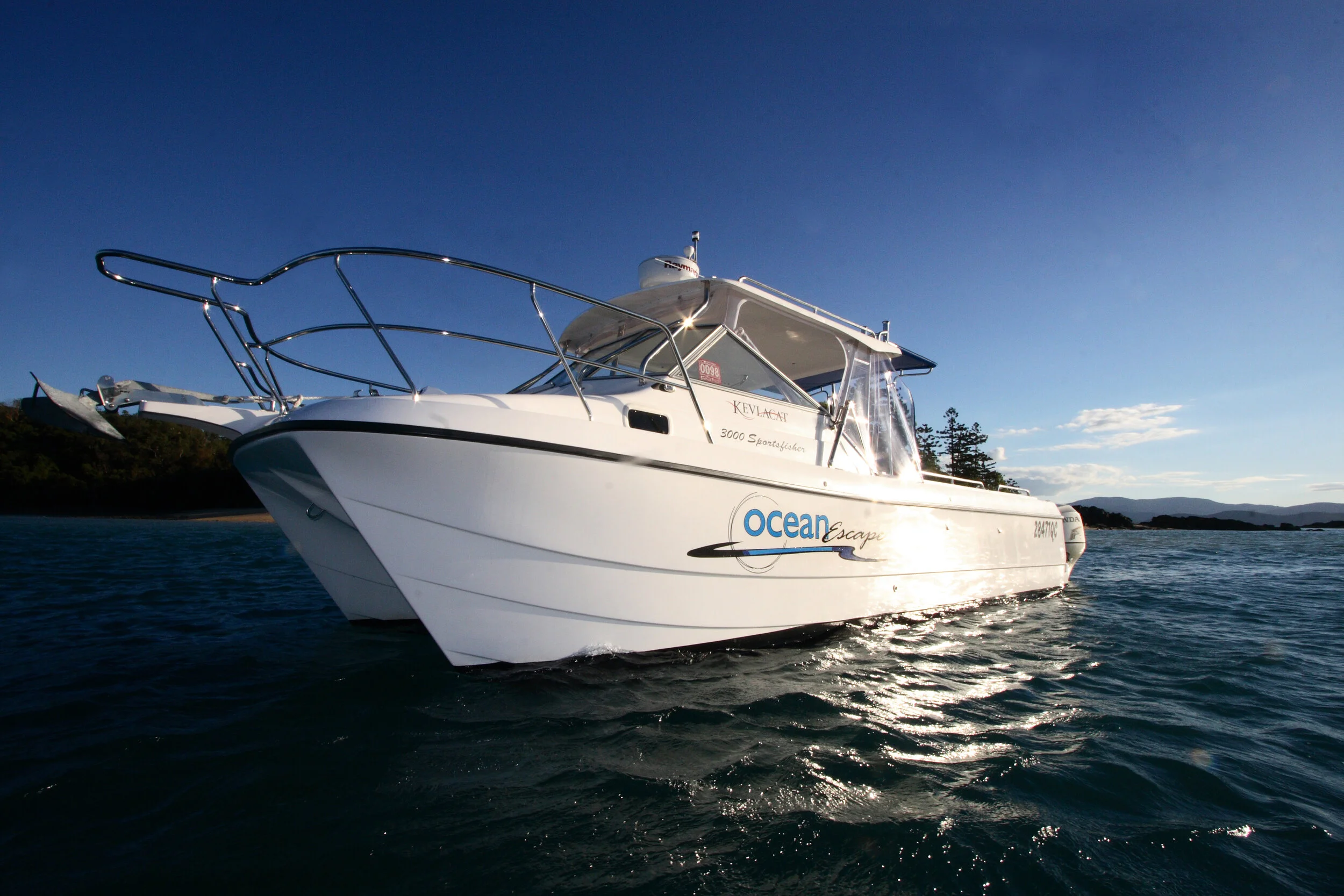 A white motorboat named Ocean Escape on water with a clear blue sky and distant land in the background.