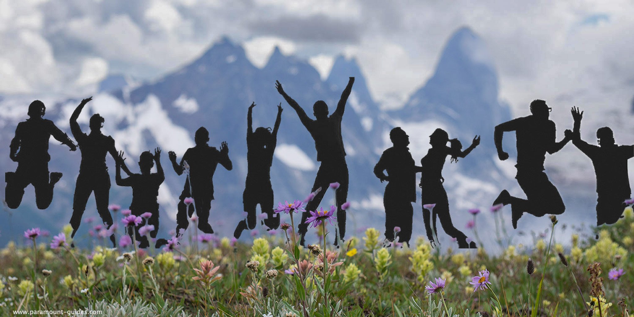 Silhouettes of people jumping and dancing in a field of wildflowers with Bugaboos Spires peaks in the background.