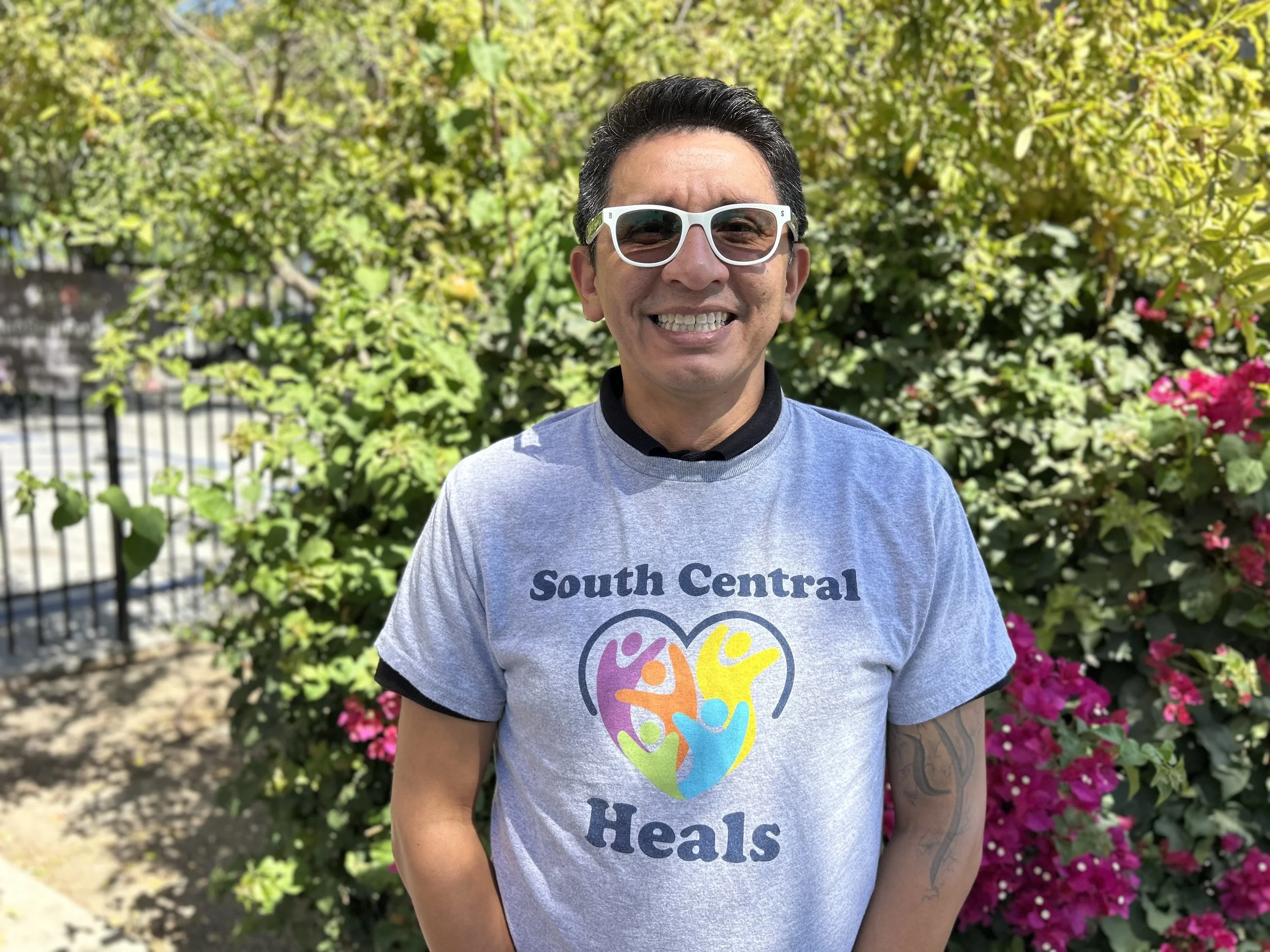 Man with short brown hair and white rimmed sunglasses smiling widely at the camera.