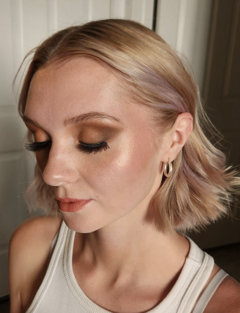 Woman with short blonde hair and makeup, wearing a tank top and earrings