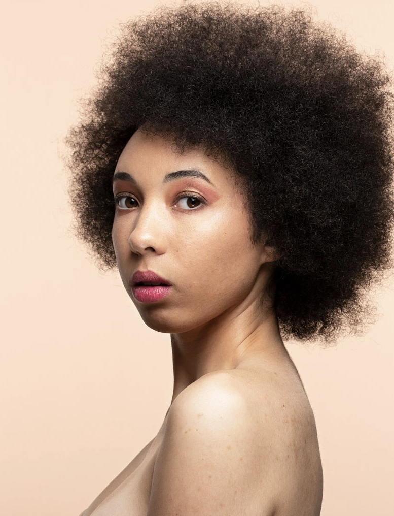 Portrait of a person with curly hair against a beige background.