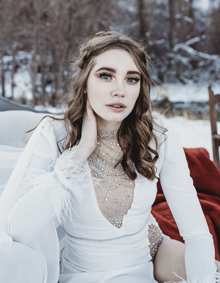 Woman in a white dress with sheer, jeweled detailing in a snowy outdoor setting.