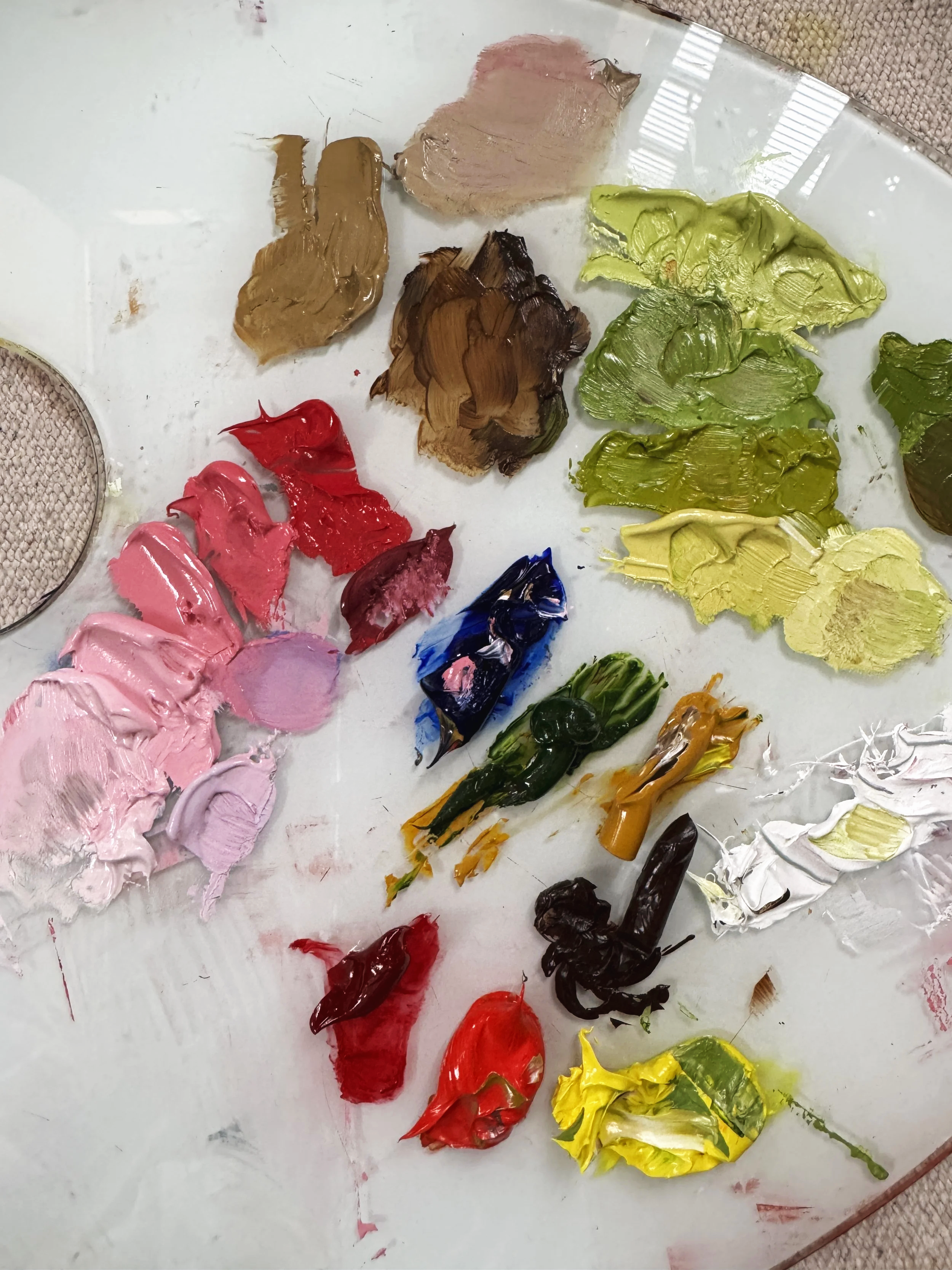 A glass painting palette with half mixed oil paints primarily in pink and green hues