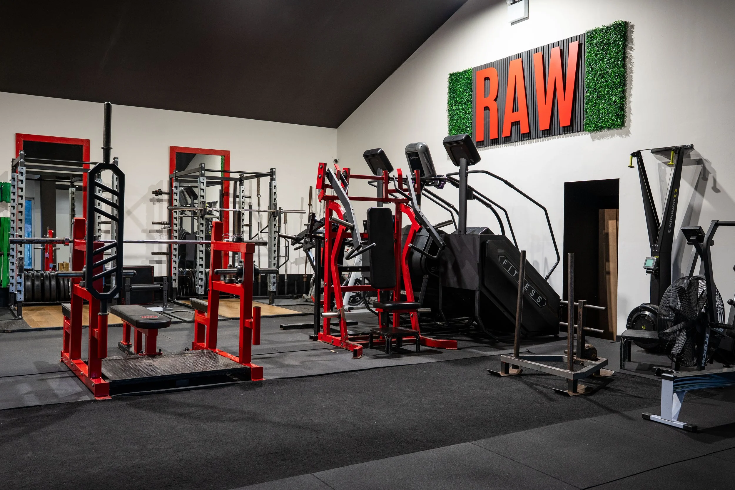 Empty fitness gym with various workout machines, weights, and equipment, and a large sign on the wall that says 'RAW' in red letters.