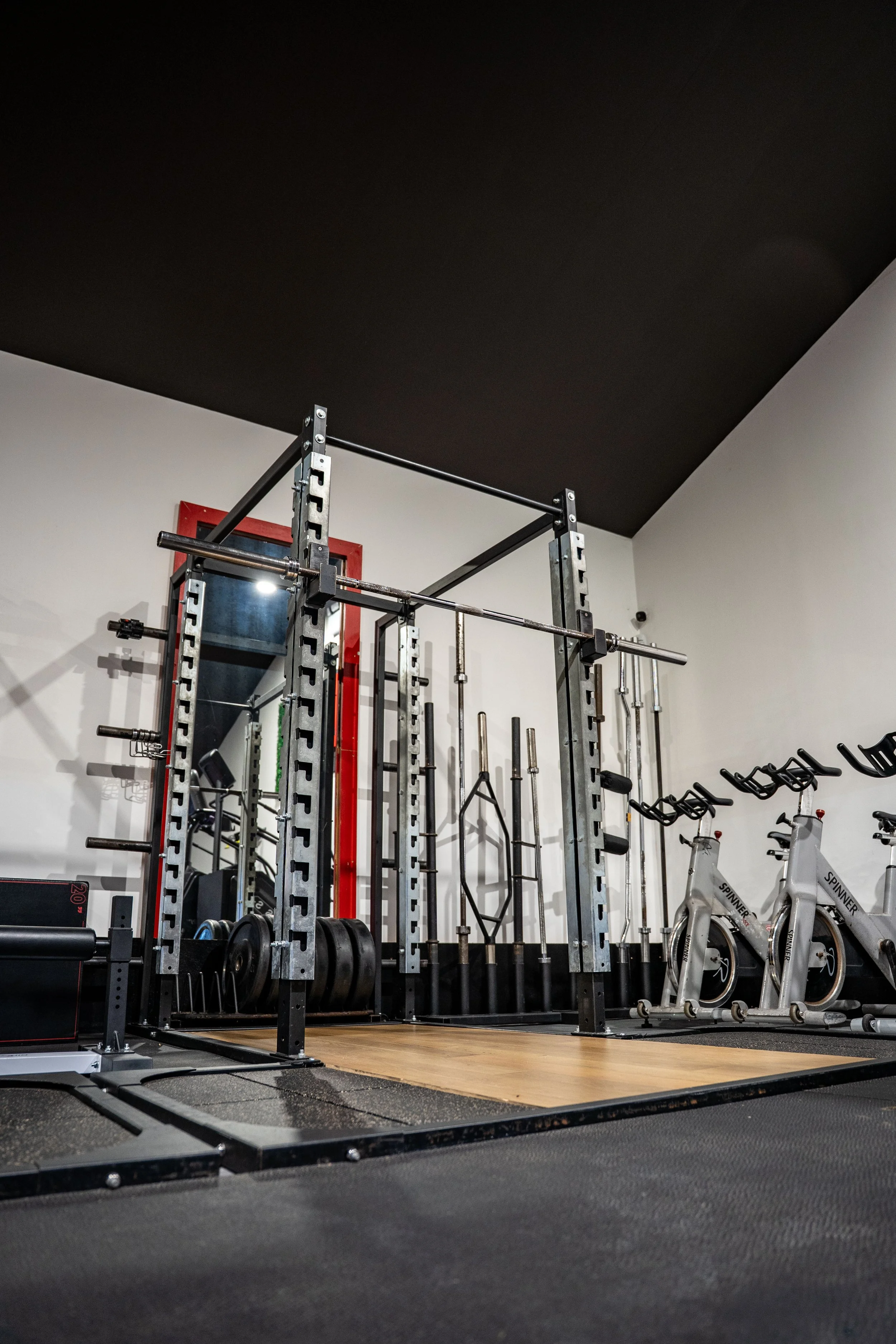 Empty gym with power rack, barbells, and exercise bikes.
