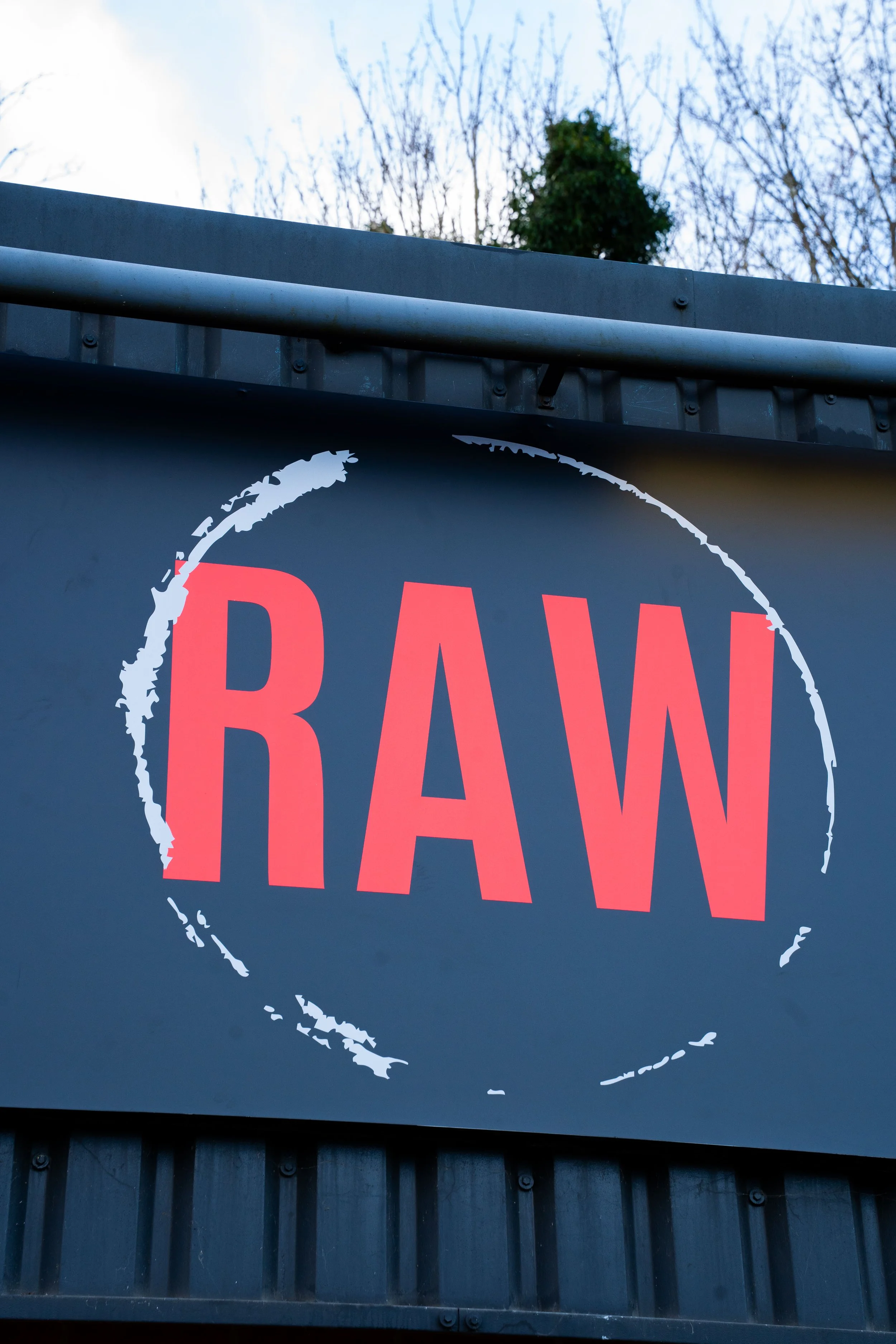 Sign with the word 'RAW' in large red letters inside a white circle outline on a dark background.