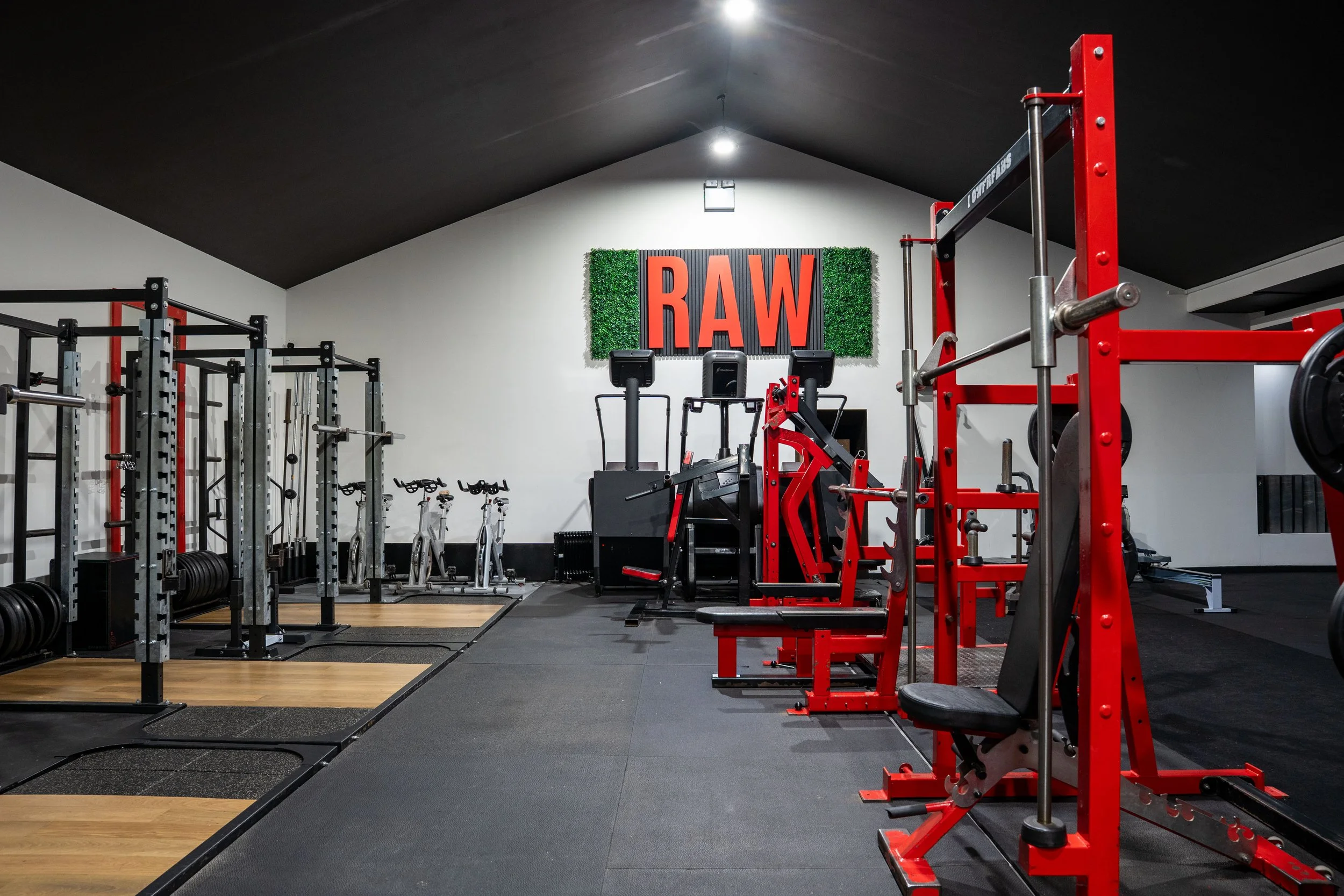 Empty gym with weightlifting equipment, cardio bikes, and a wall decoration with the word 'RAW' in large letters.
