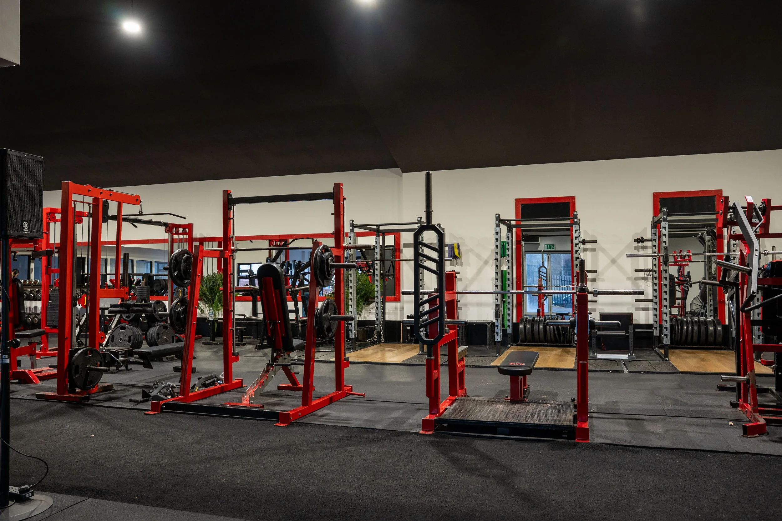 Empty gym with red and black weightlifting equipment and mirrors on the walls.