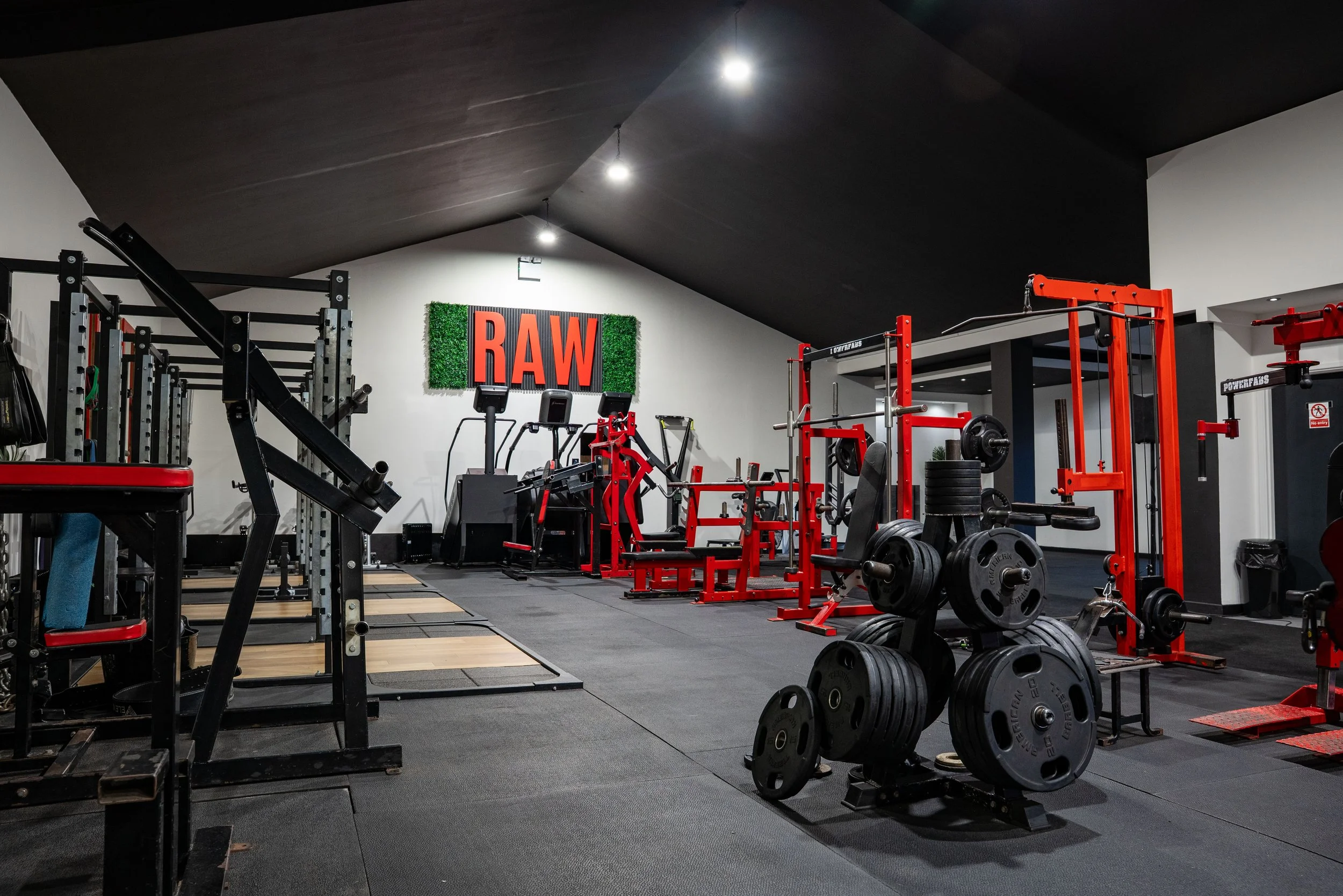 Empty gym with weightlifting equipment, cardio machines, and a large "RAW" sign on the back wall.