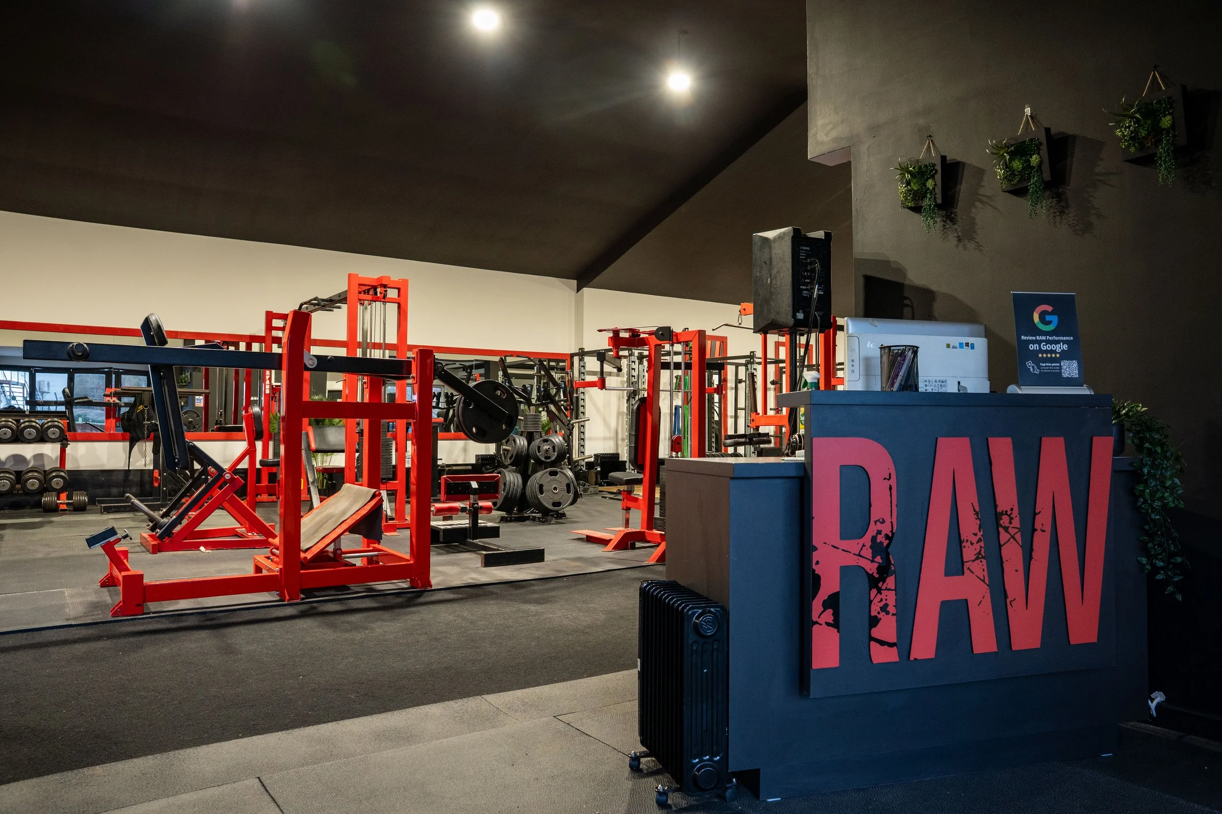 Interior of a gym with various red weightlifting equipment, black weight plates, and a reception desk with the word 'RAW' on it.