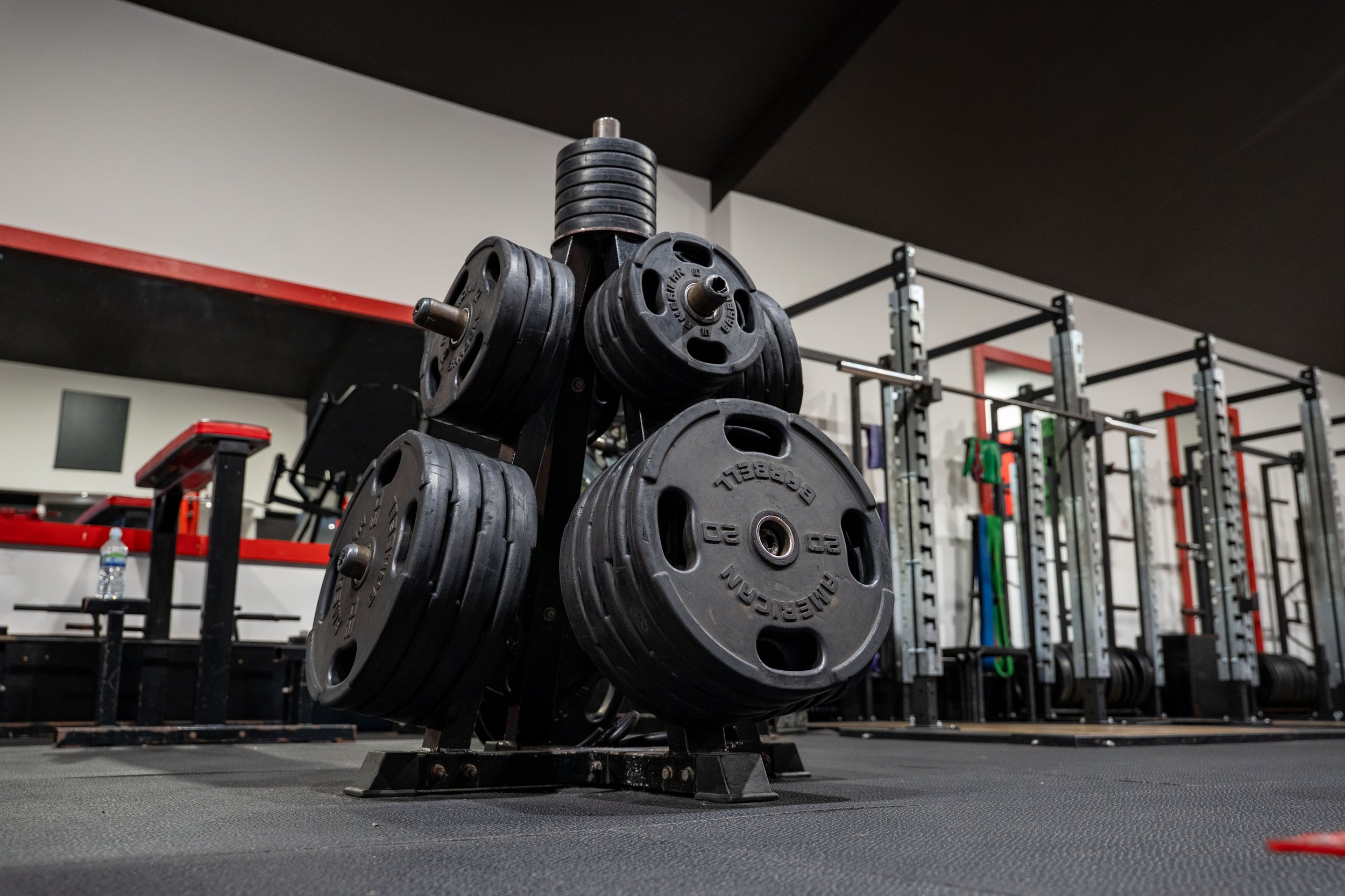 A rack of black weight plates in a gym with workout equipment and racks in the background.